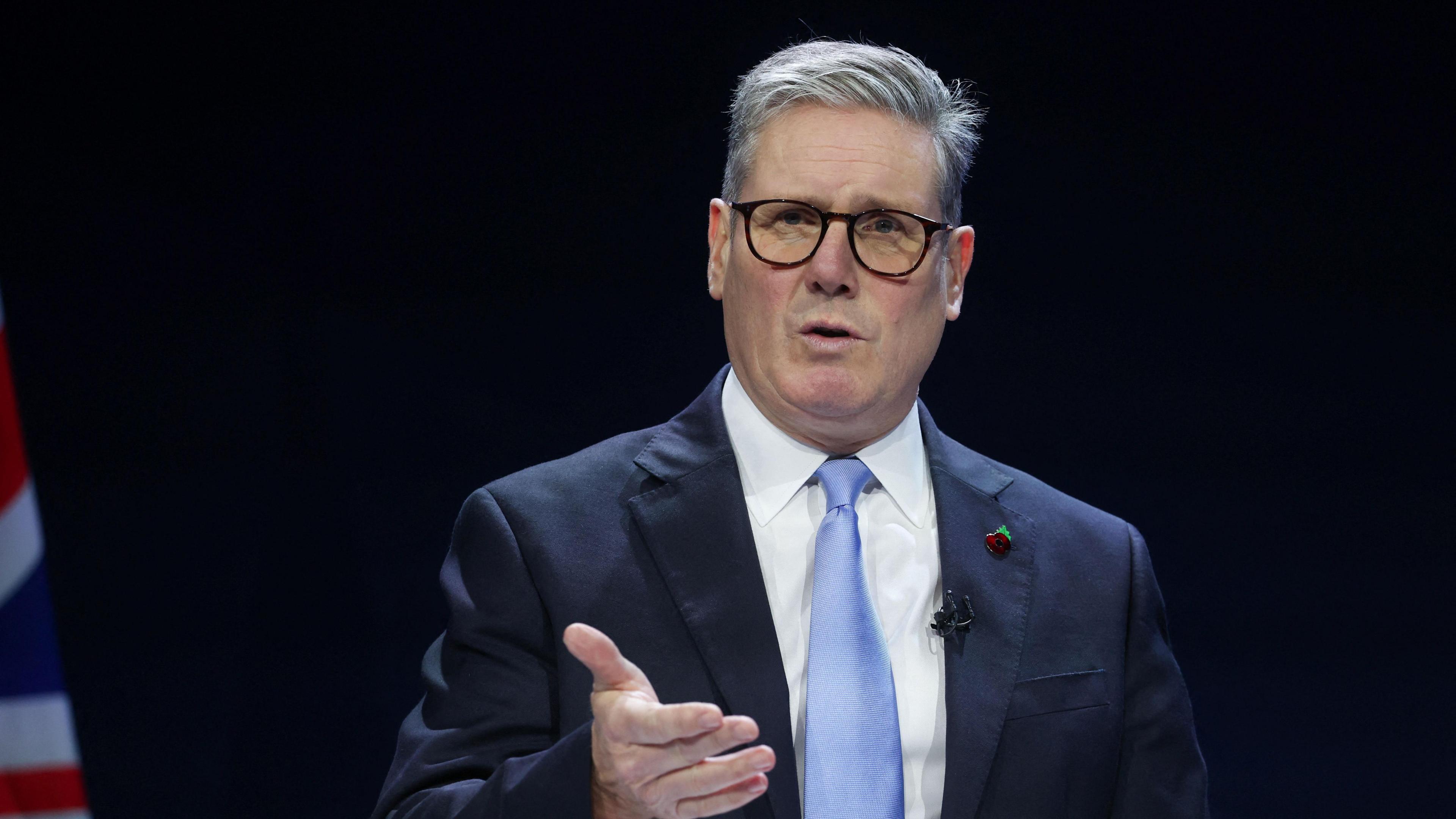 Sir Keir Starmer in a dark blue suit and blue tie with black glasses making a speech