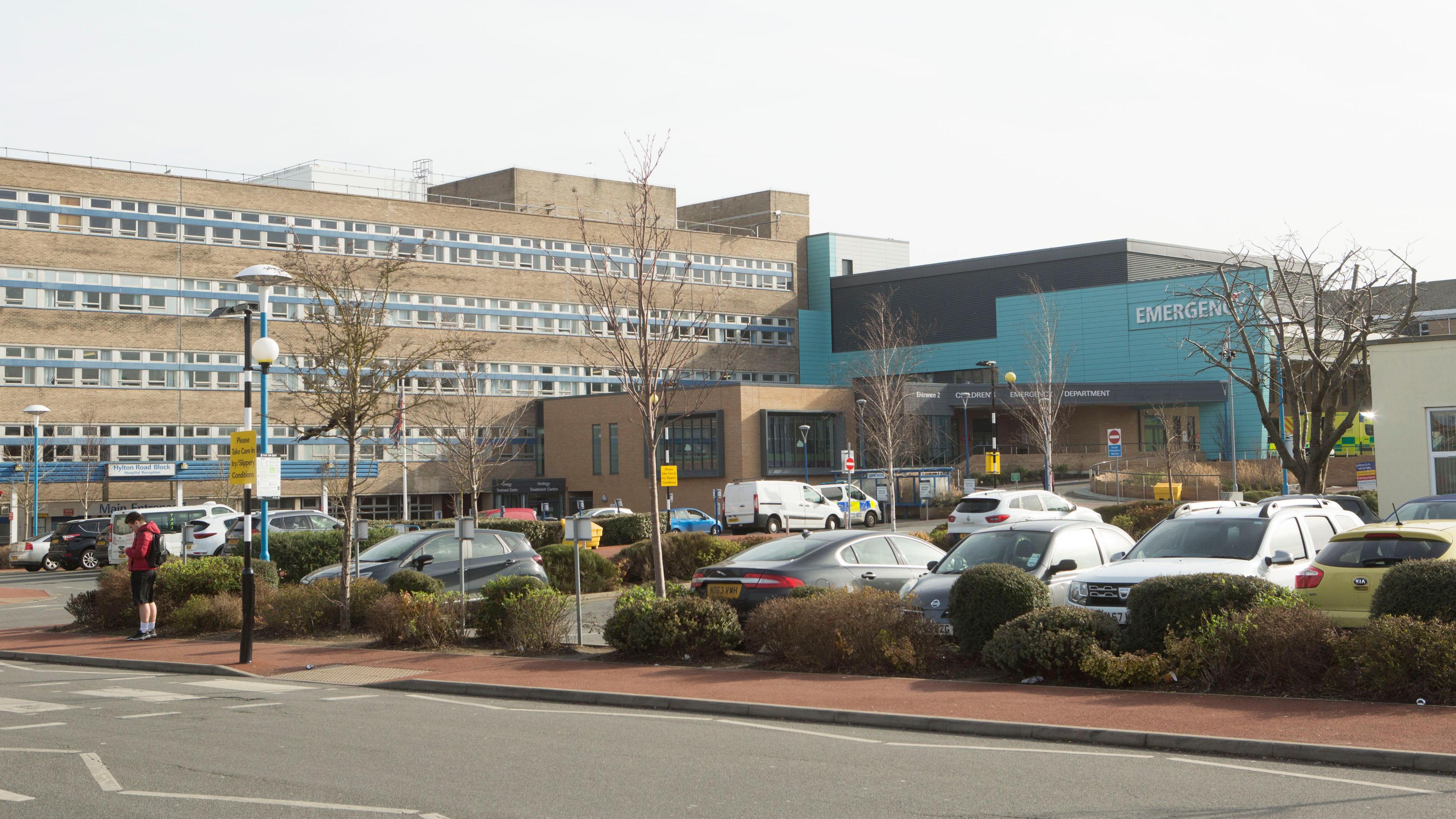 Sunderland Royal Hospital is a five-storey brick building with rows of windows. A section of the building, which is blue, juts out. There is also a car park out front.