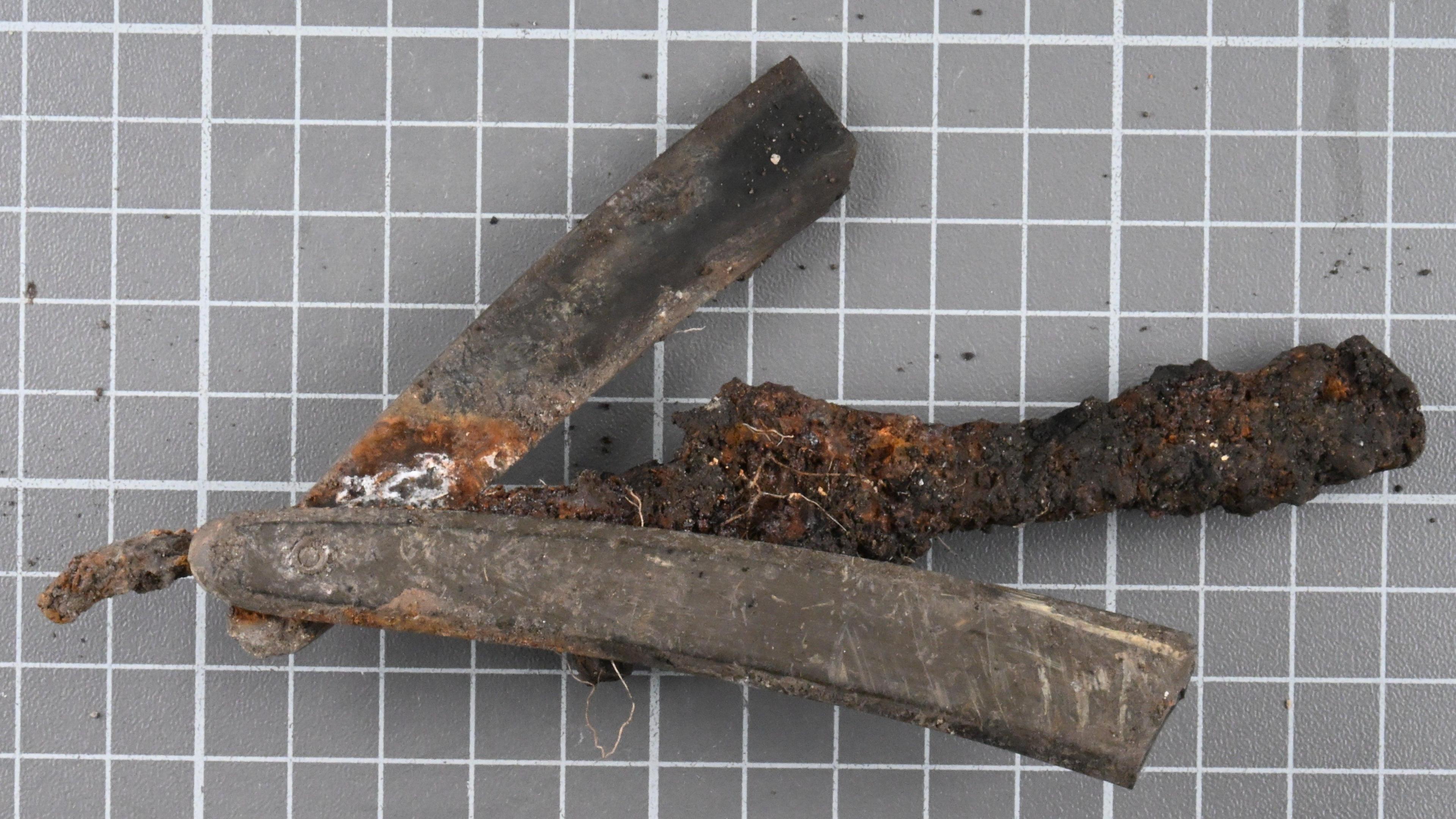 A historic razor found during an excavation. It is brown and heavily rusted in places. 