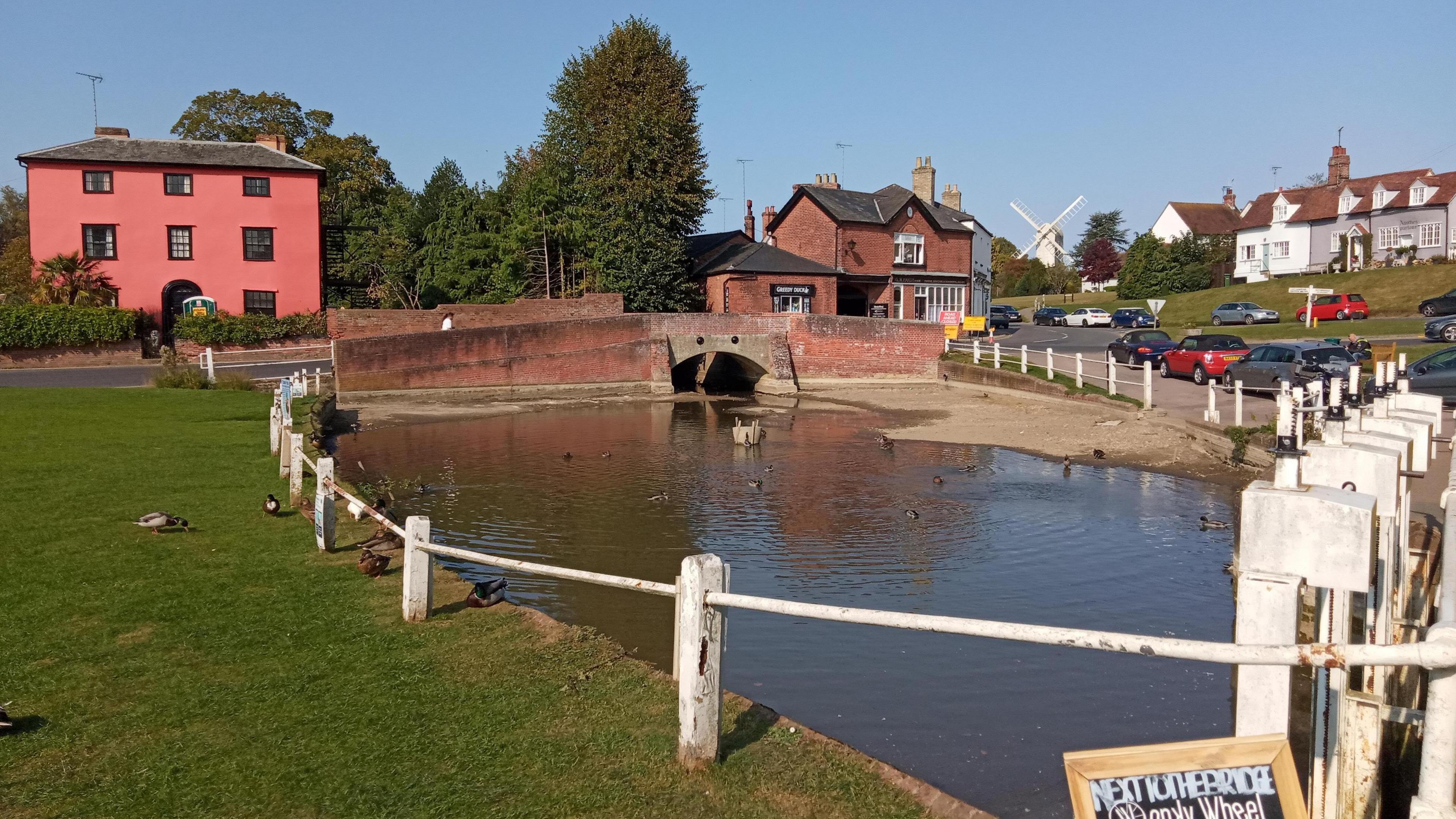 The pretty village green in Finchingfield, which has houses dotted around it and a pond in the middle with a brick bridge crossing it.