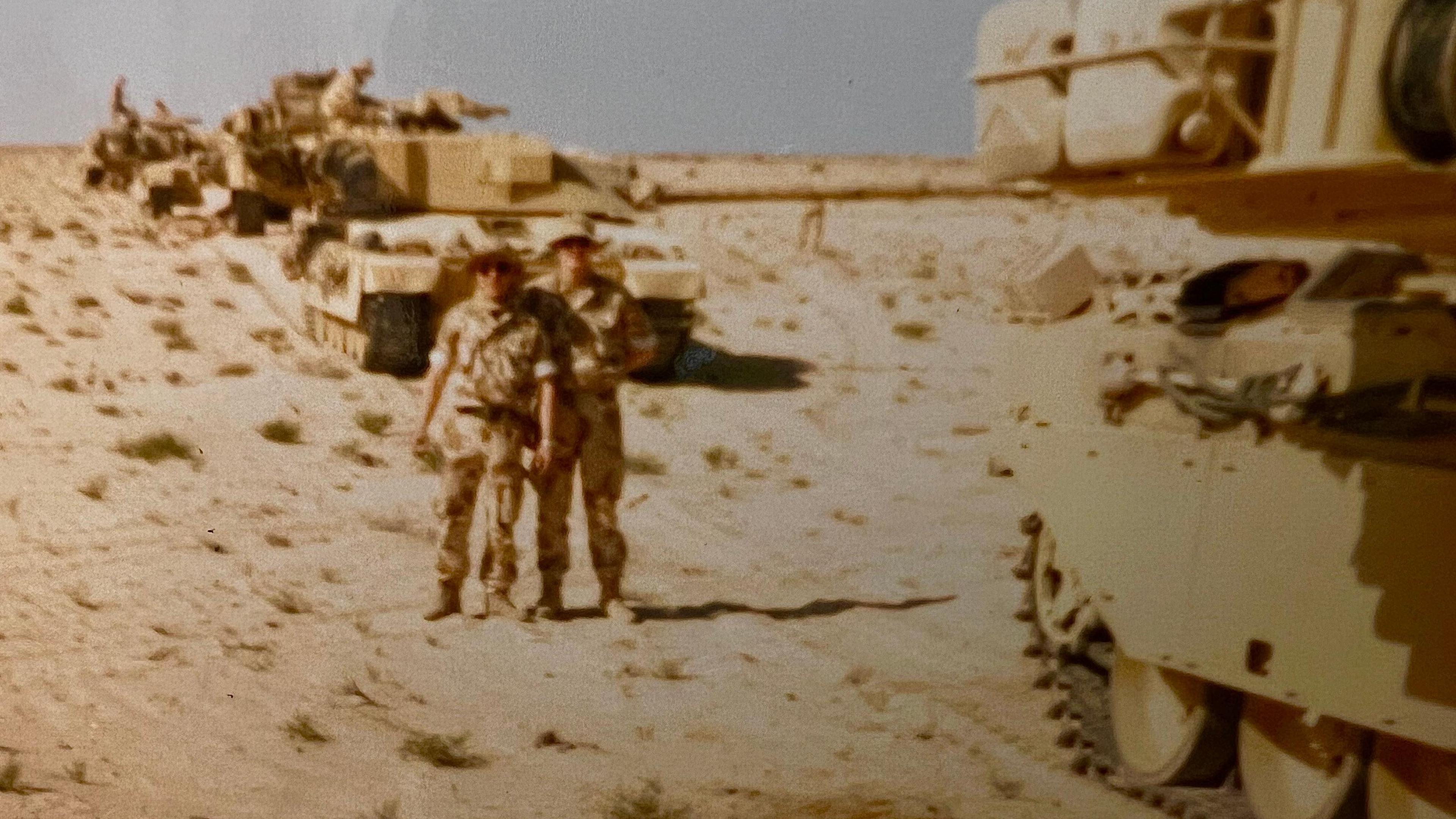 Darren Horvath alongside a colleague and military vehicles in a desert