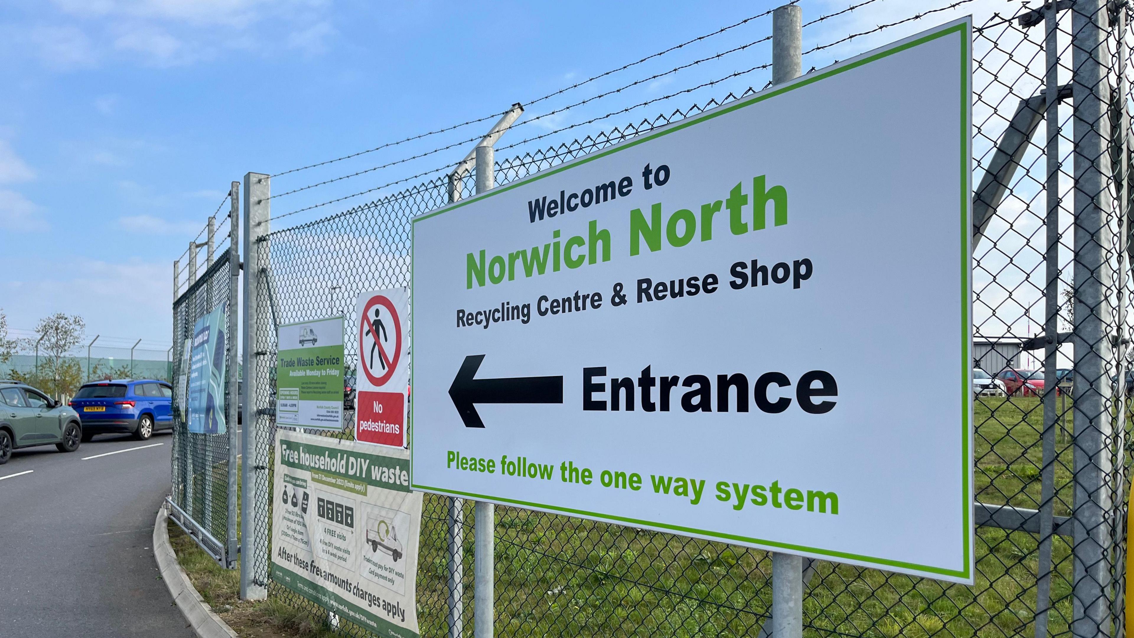 A white and green sign which reads, Welcome to Norwich North Recycling Centre and Reuse Shop. Entrance. Please follow the one way system.