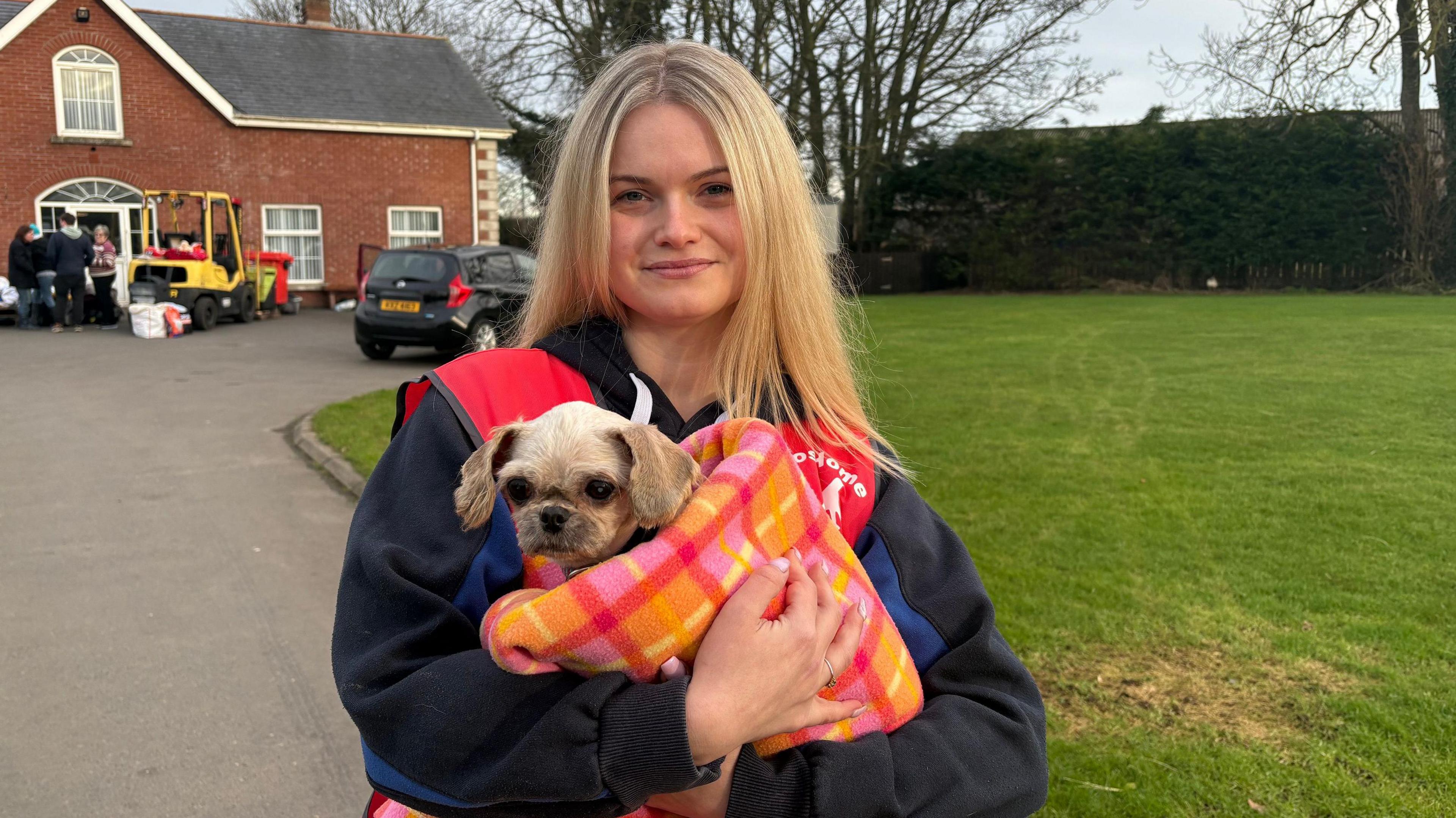 Holly McConnell who volunteers at Almost Home Animal Rescue NI, holding Dorothy the dog. Holly has long blonde hair, holding Dorothy who is cream coloured with big ears and wrapped in an orange and pink blanket.