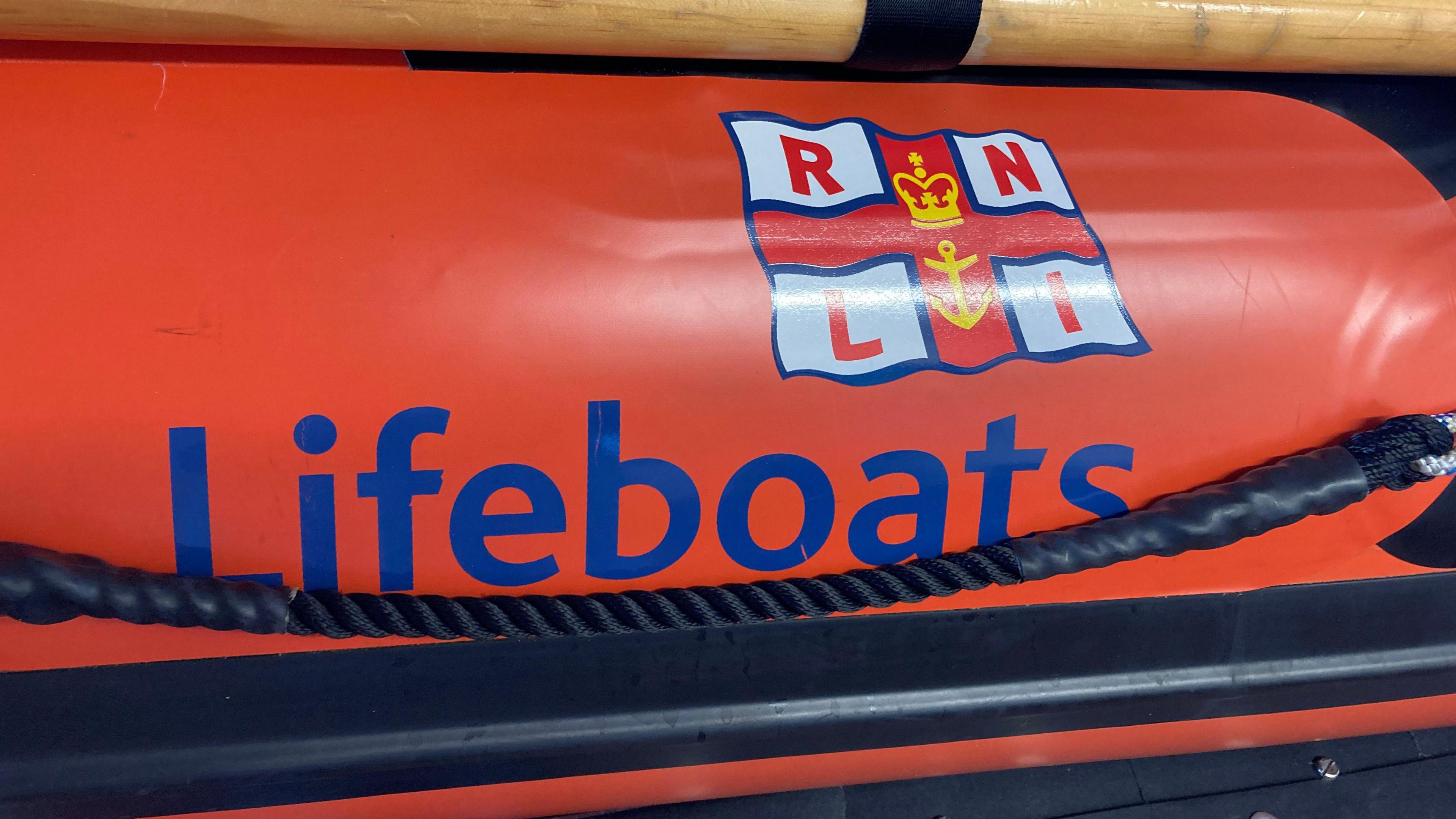 An RNLI flag with the word lifeboats next to it in blue, on an orange background.