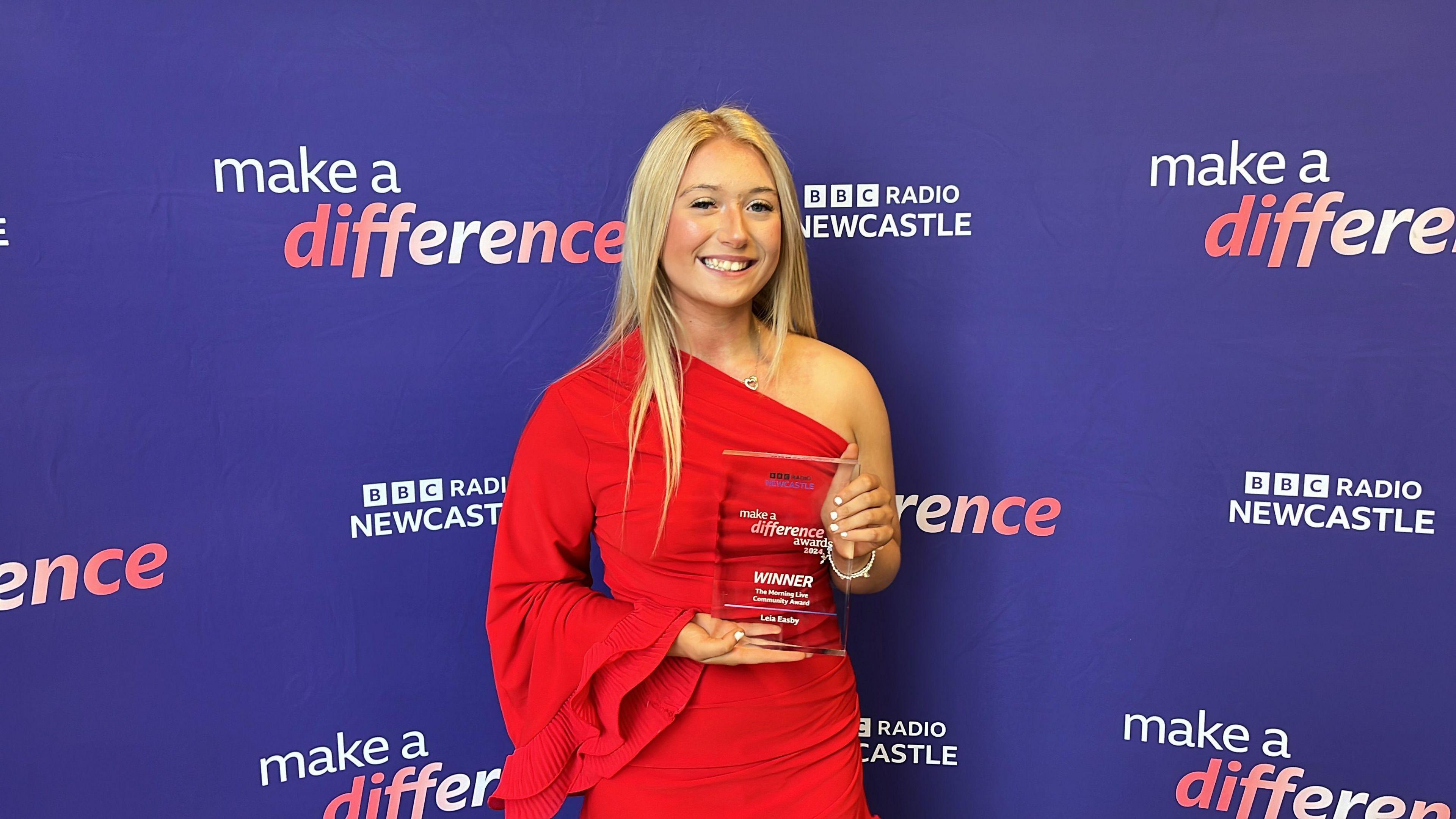 Leia Easby holding her award. She has blonde hair and is wearing a red dress.