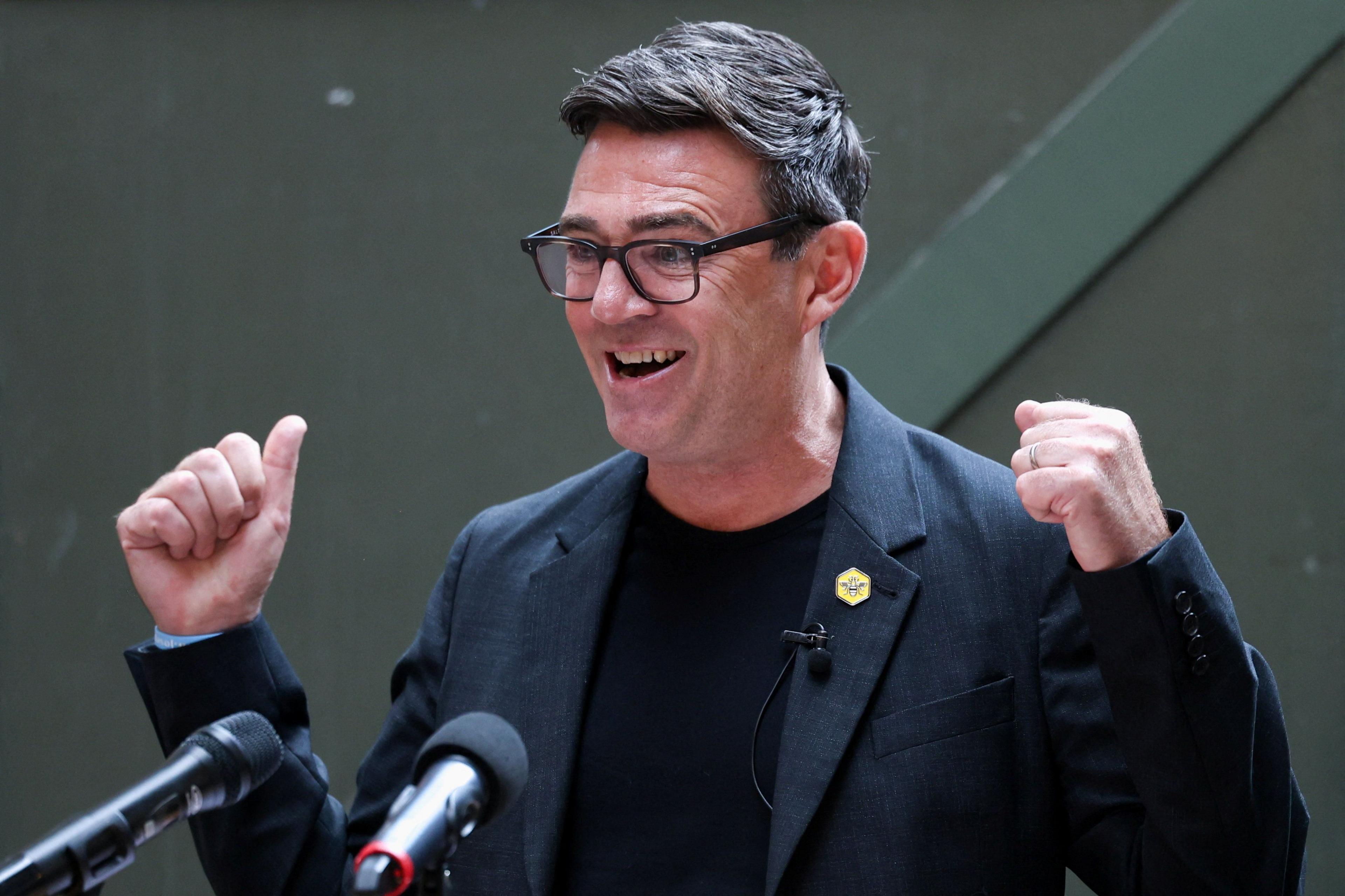 Andy Burnham, wearing a black jacket and t-shirt, stands at a podium.