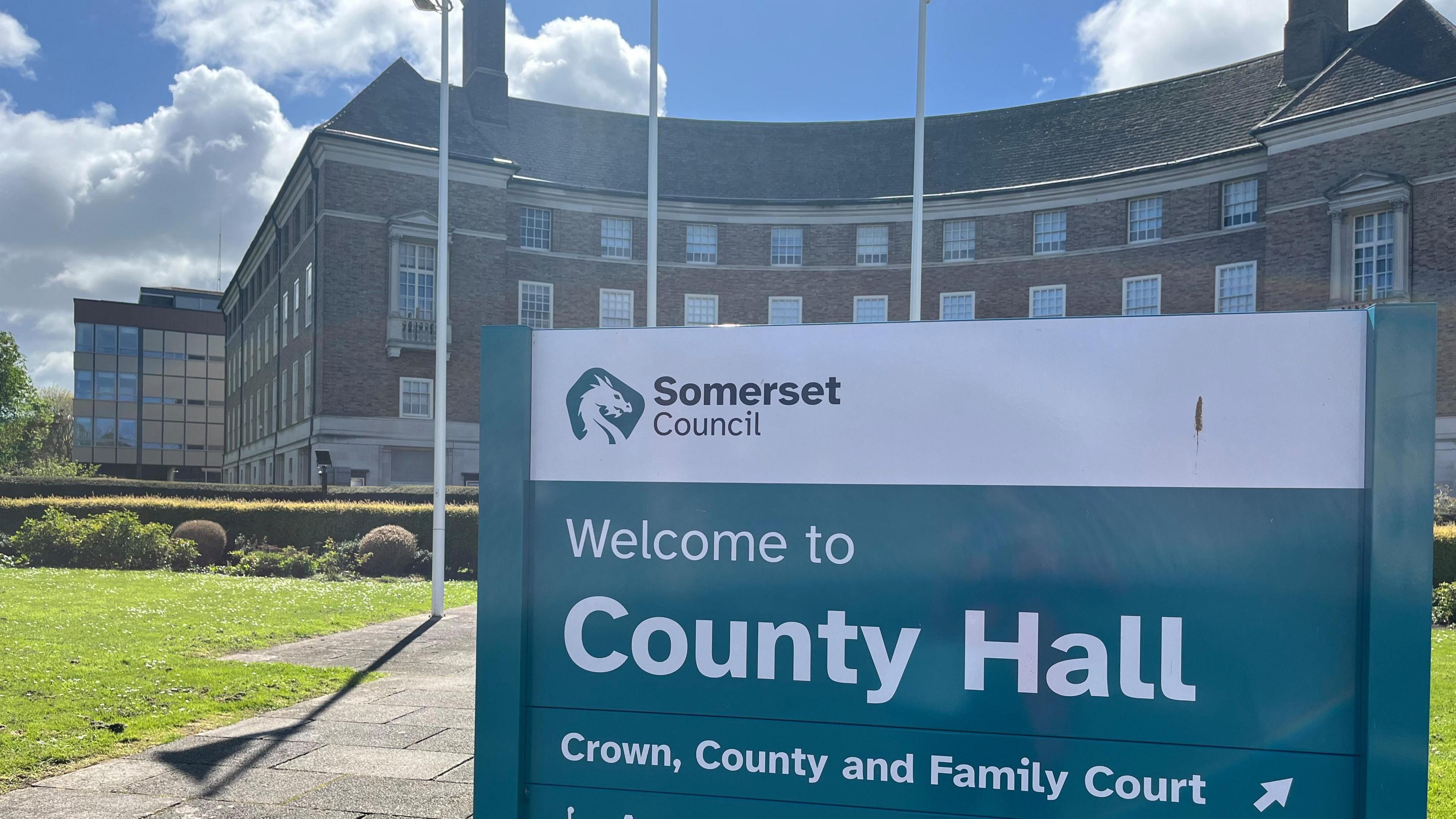 A view of Somerset Council's County Hall with a green sign in the foreground.