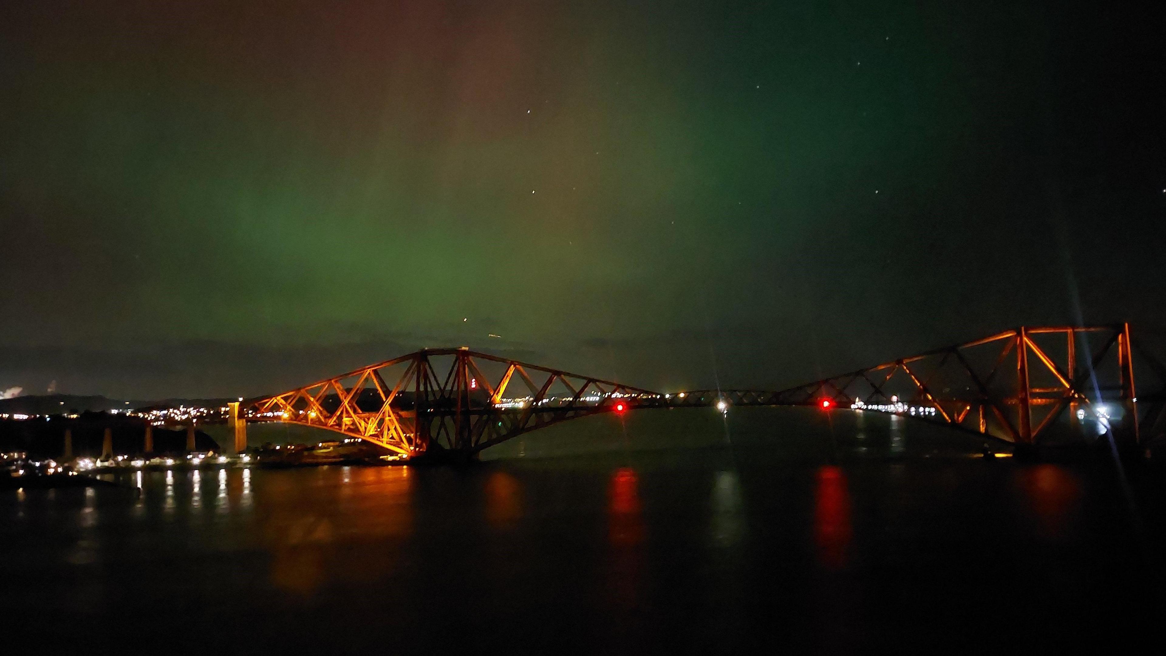 The Forth Bridge taken from the road bridge. There is green and pink aurora above.