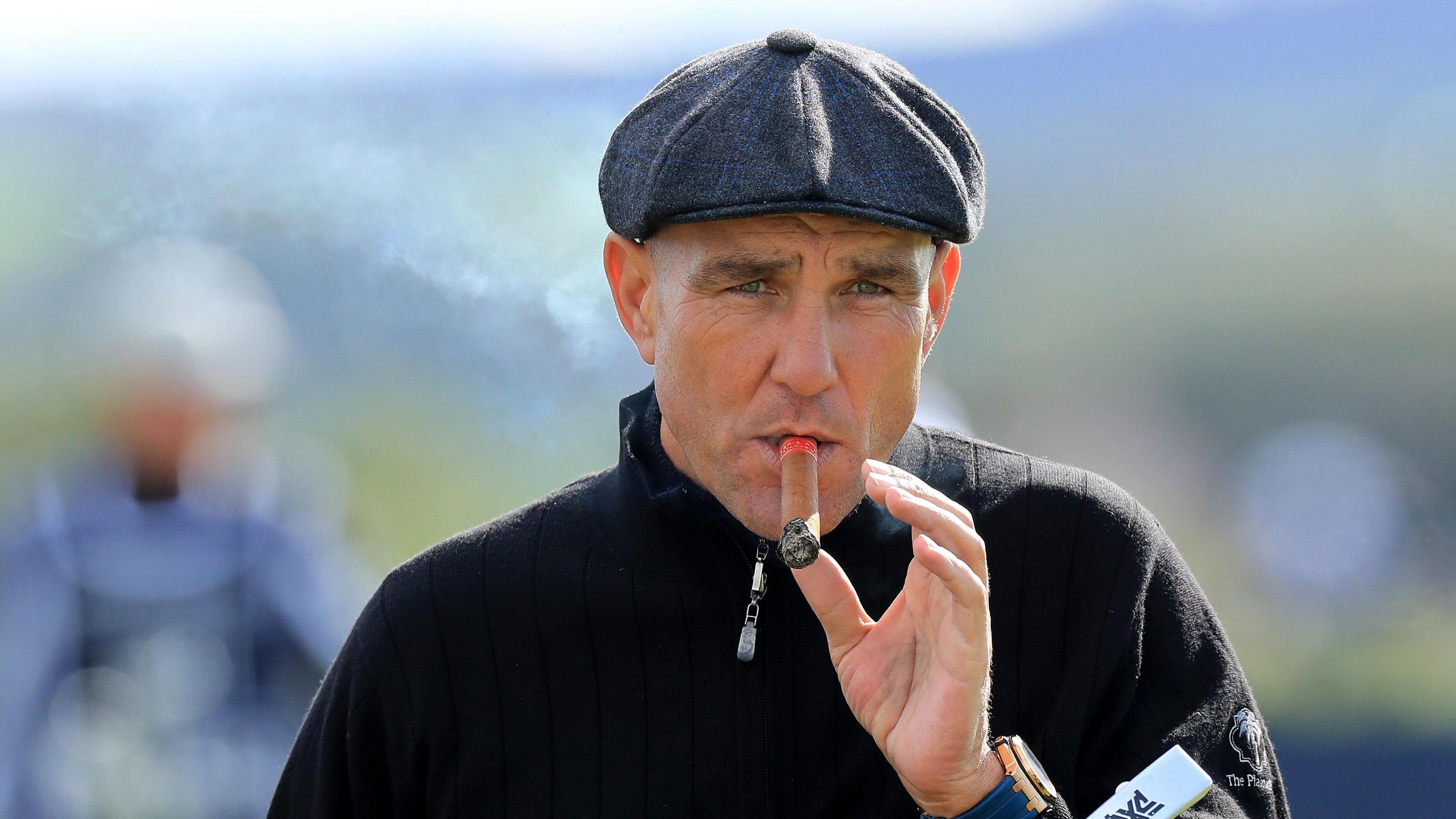 Vinnie Jones pictured wearing a flat cap and smoking a cigar.