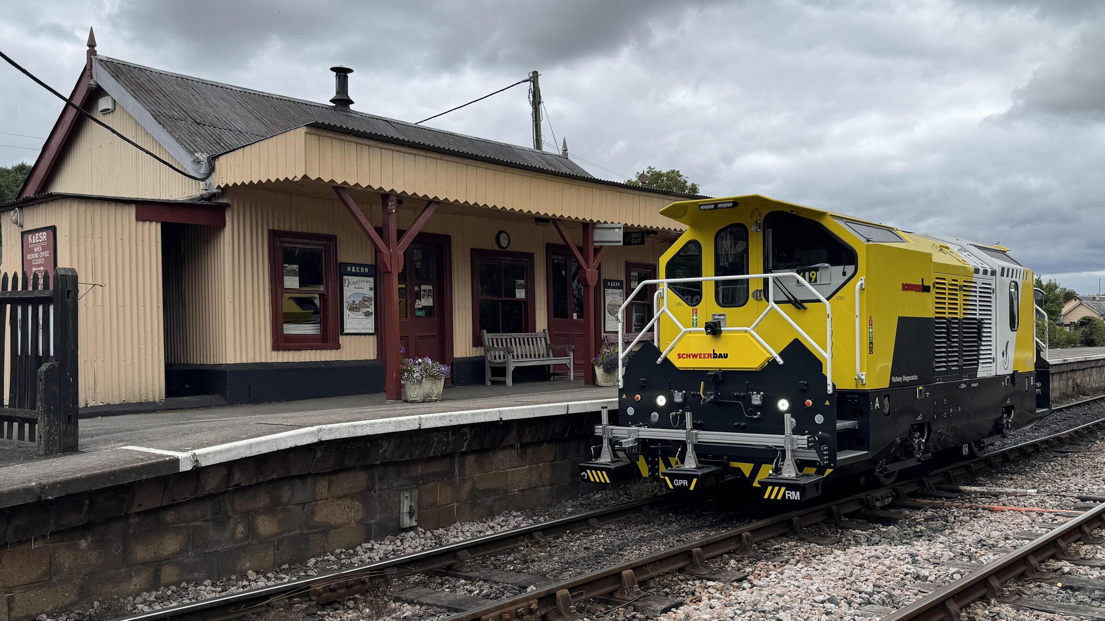 A yellow maintenance train outside a small, brown, wooden station.