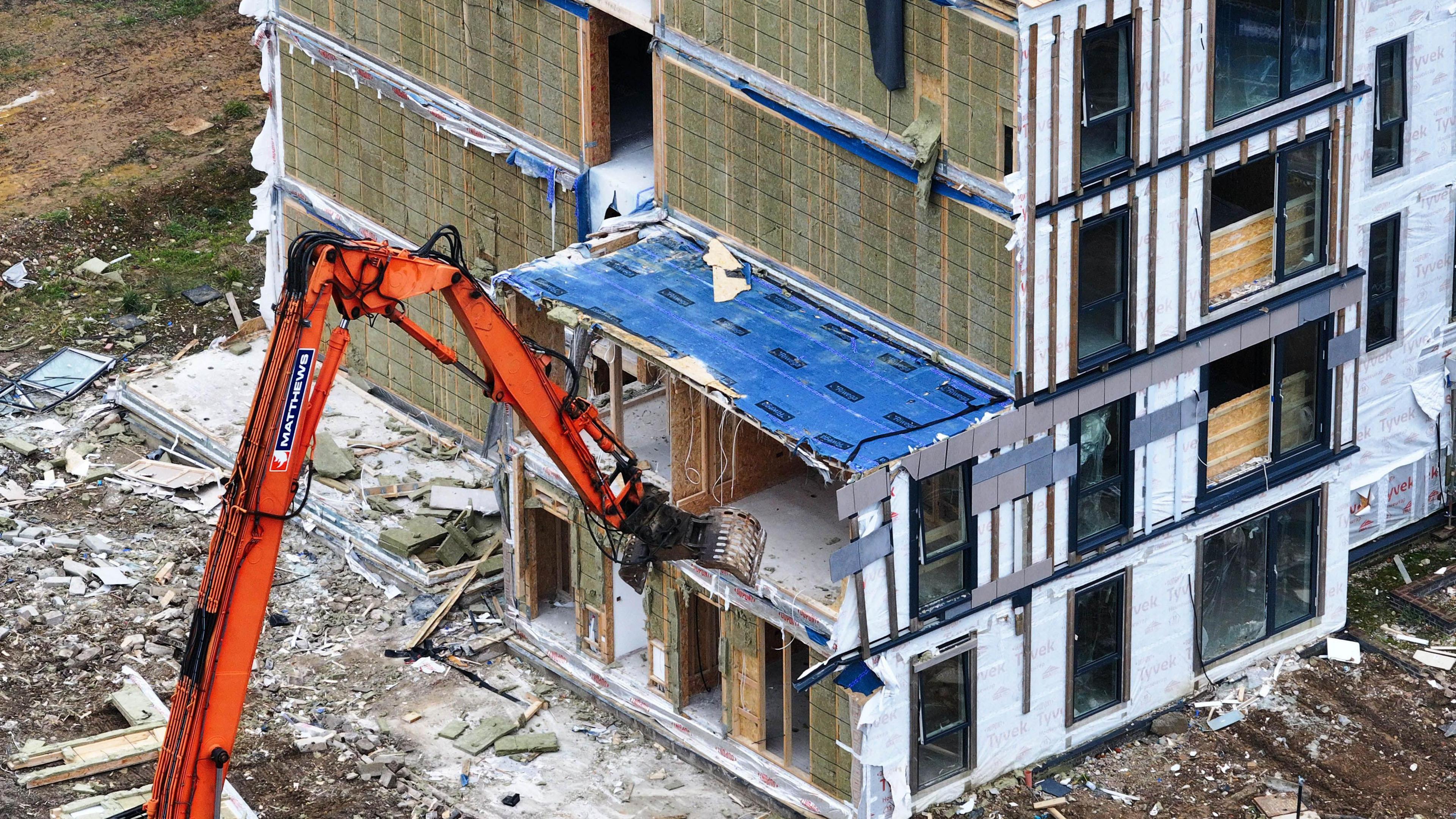 An orange digger tearing chunks from a block of flats