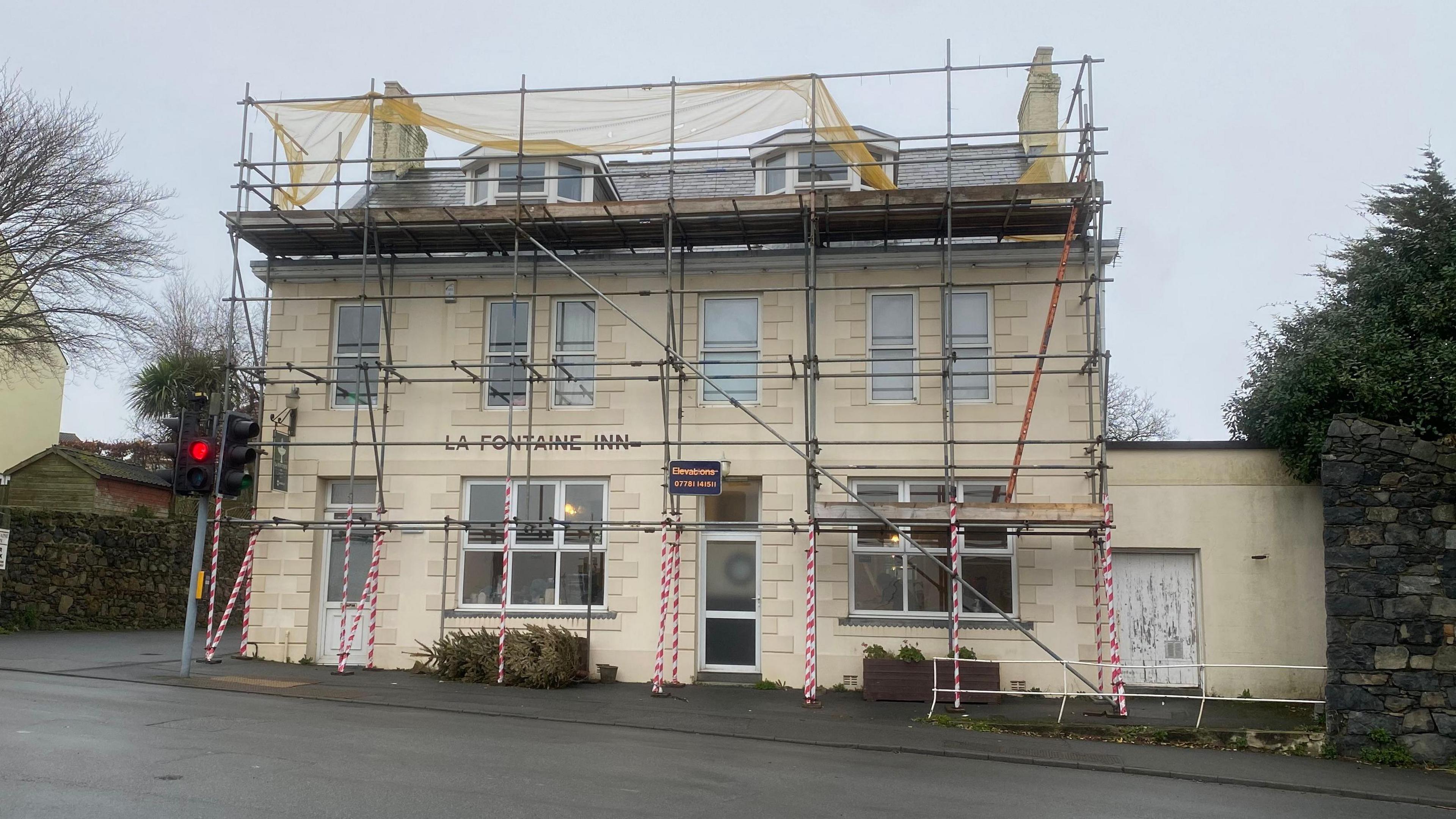 An outside view of the pub. The building looks like an old house, painted cream. There is scaffolding around the building. 