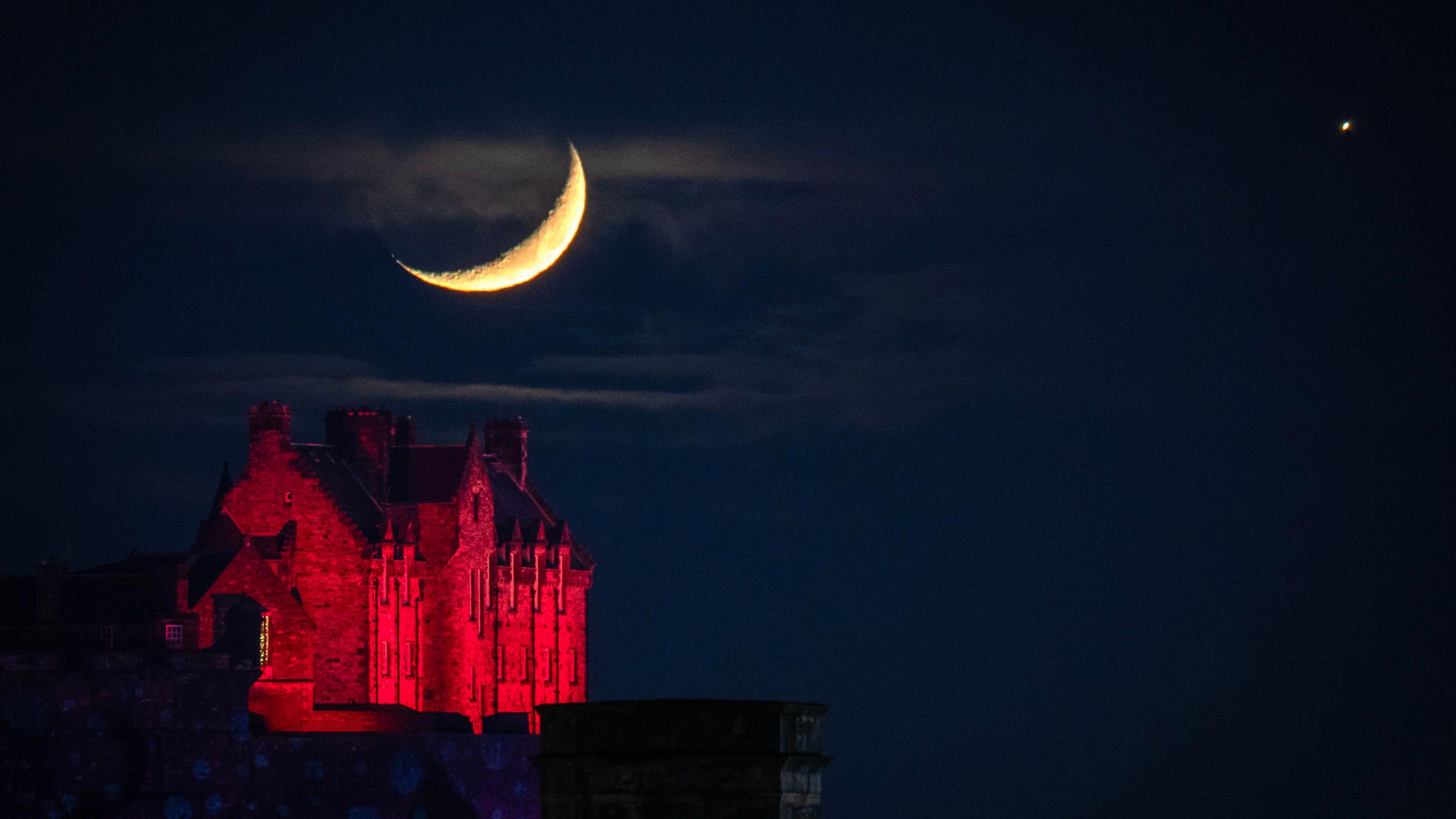 The waxing Moon and Venus above Edinburgh Castle., which is illuminated with red light