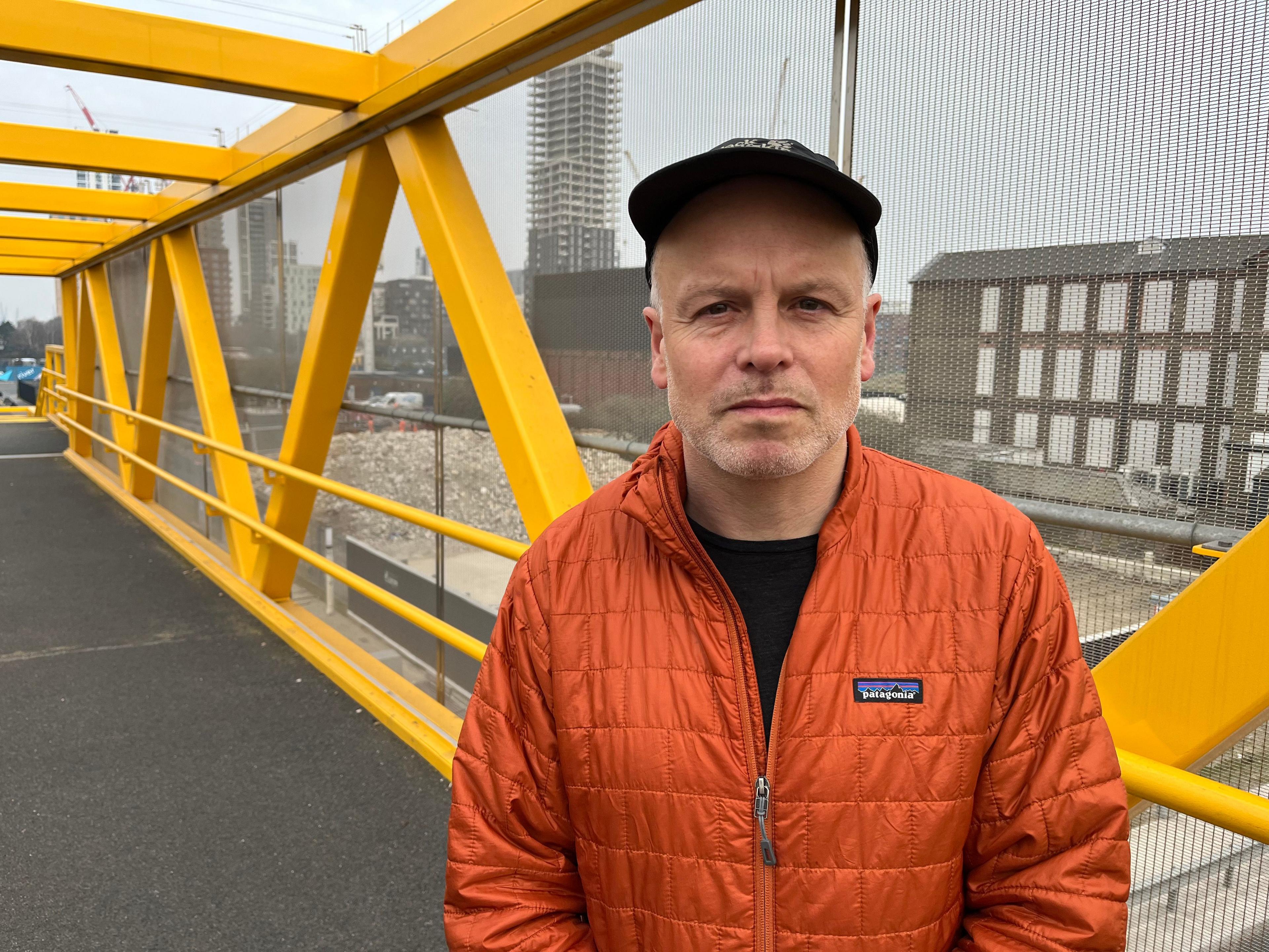 A man in a baseball cap stands on a bridge