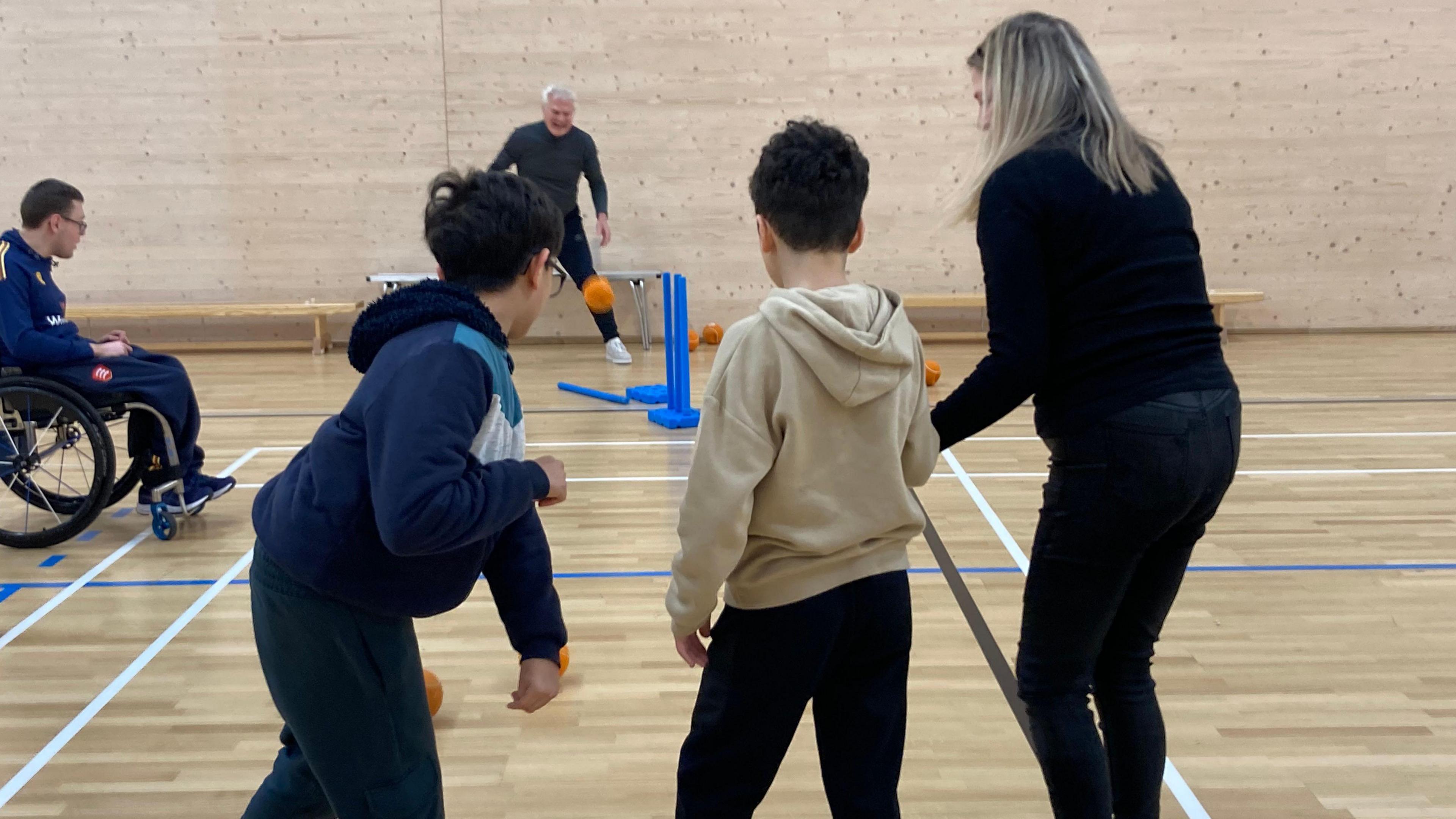 The group play cricket together, taking it in turn to throw and bat the ball.