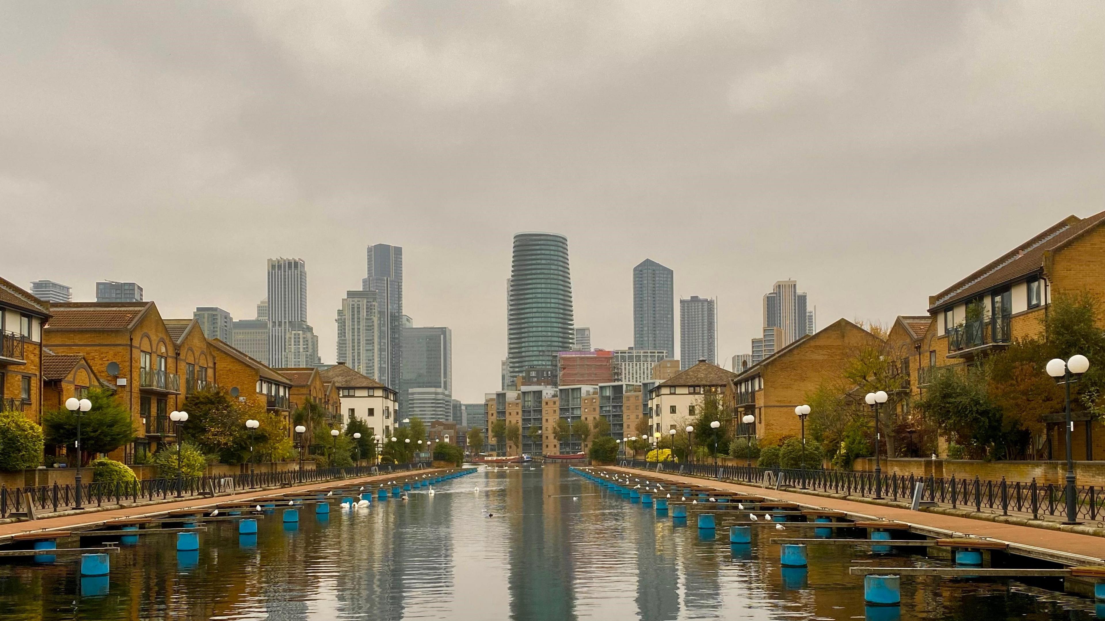 Housing either side of a former dock, with the skyscrapers of a business district in the background reaching into a grey sky