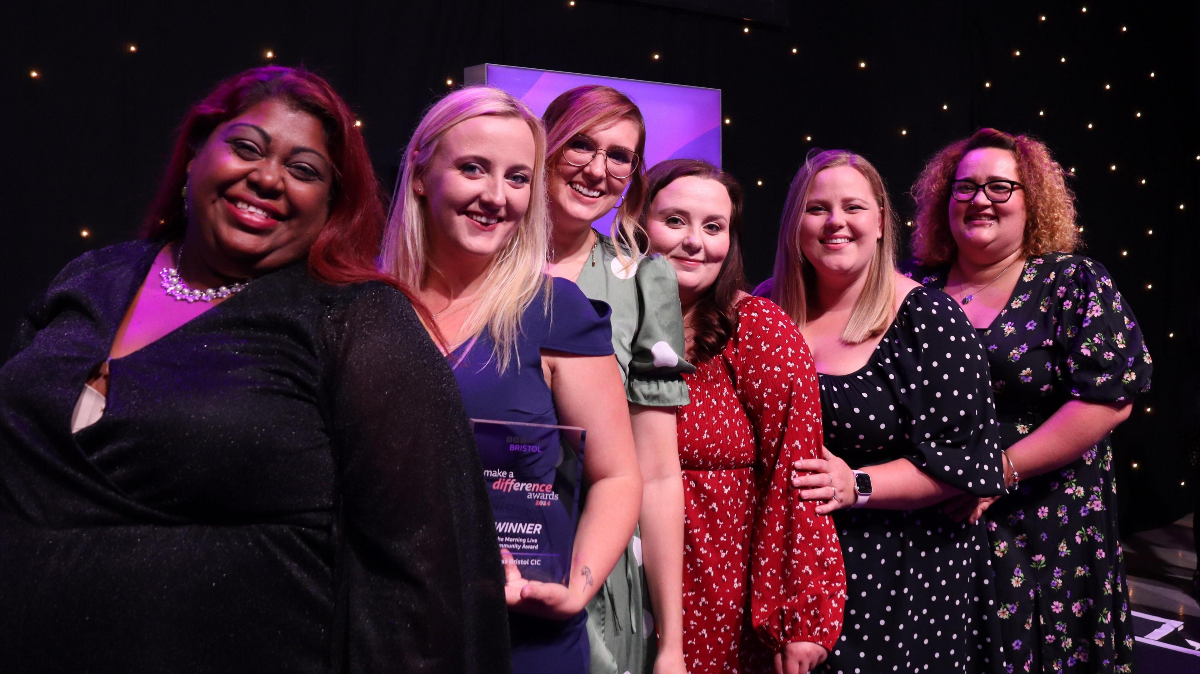 The Mamas Bristol team standing behind each other on a stage in colourful dresses.