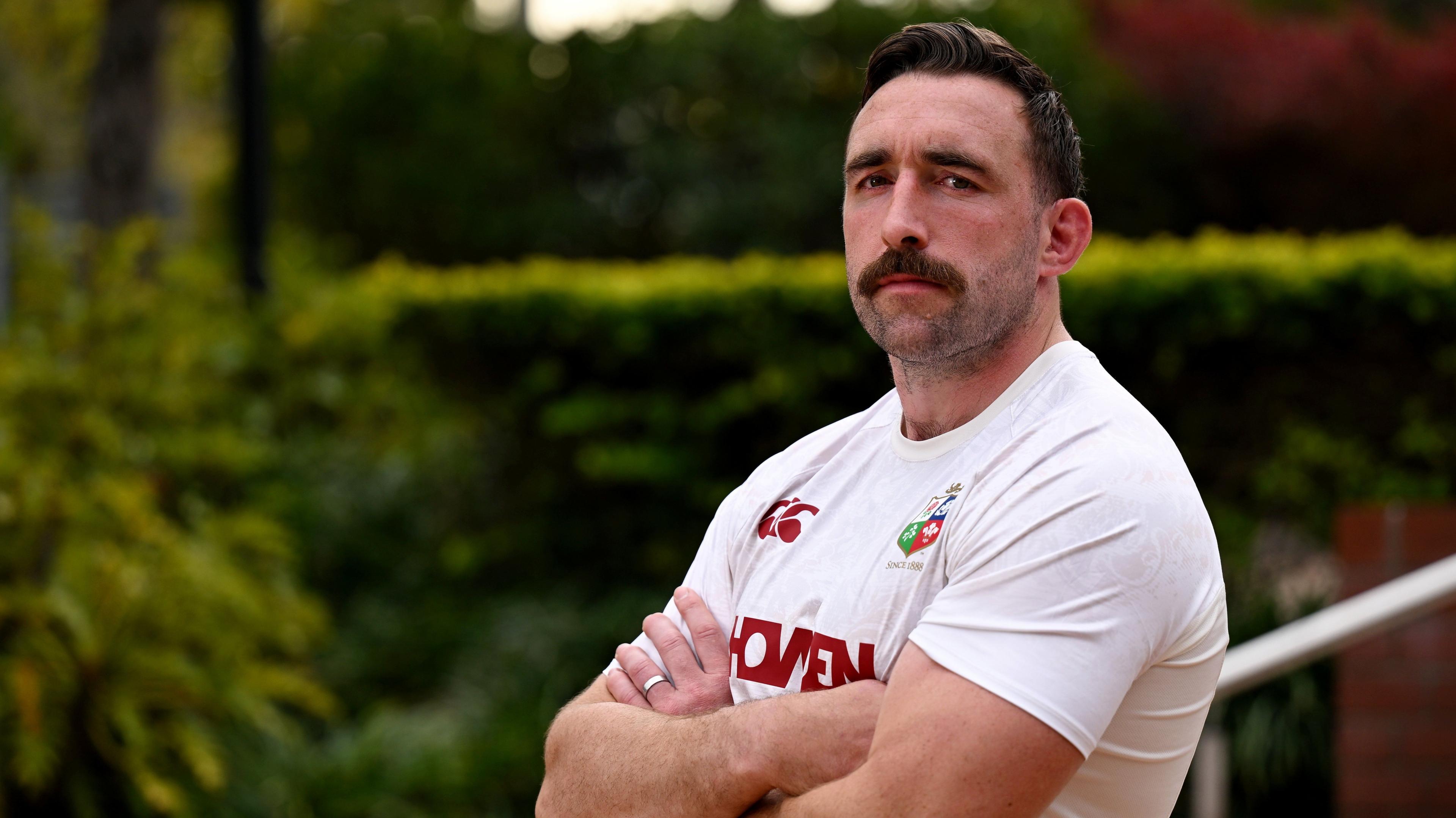 Jack Conan stands side on to the camera, arms folded across his chest, looking towards the lens