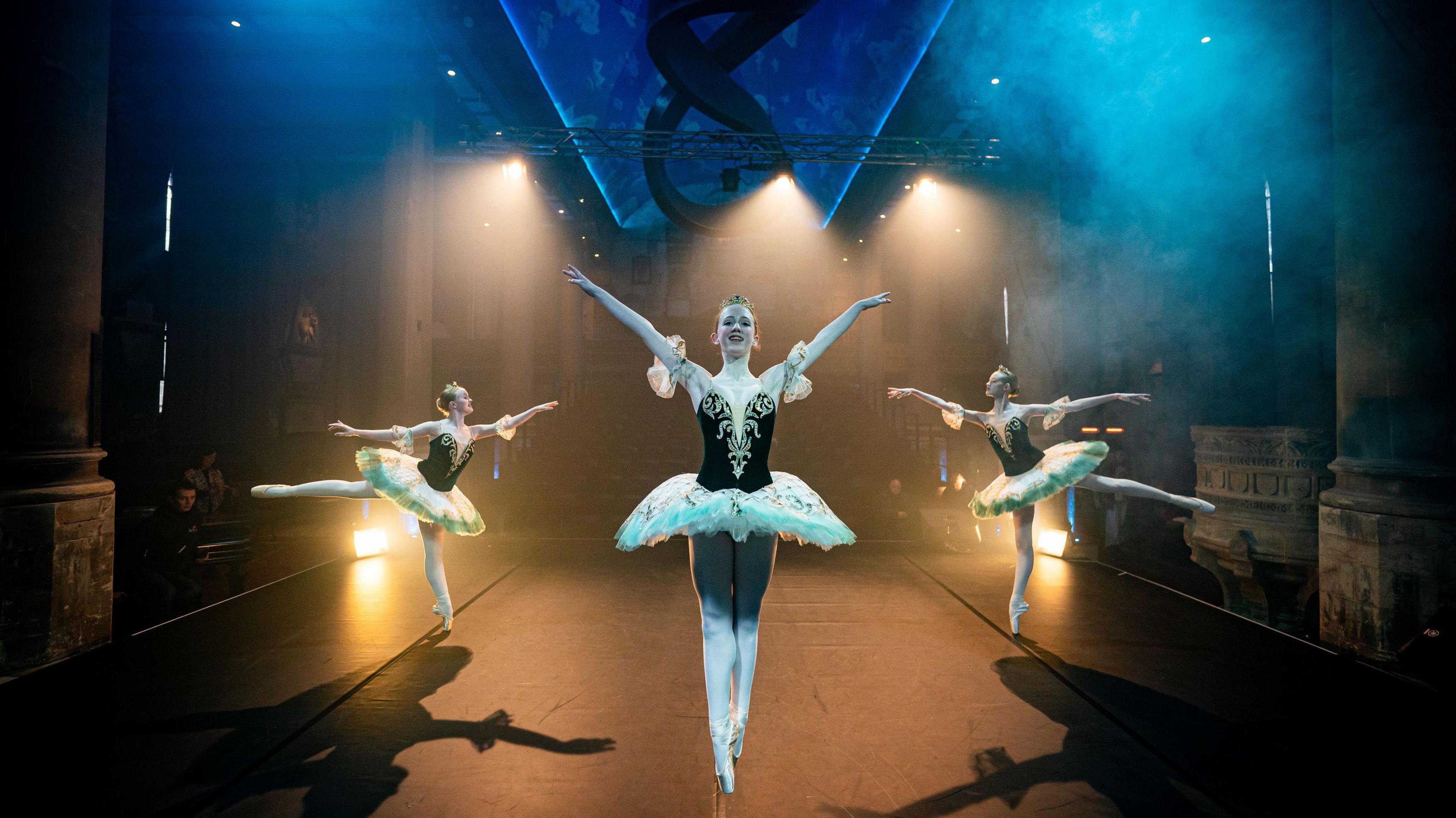 Three ballerinas in black and white outfits perform dance moves on stage at The Mount Without in Bristol. They are casting shadows due to spotlights and there is dry ice in the air