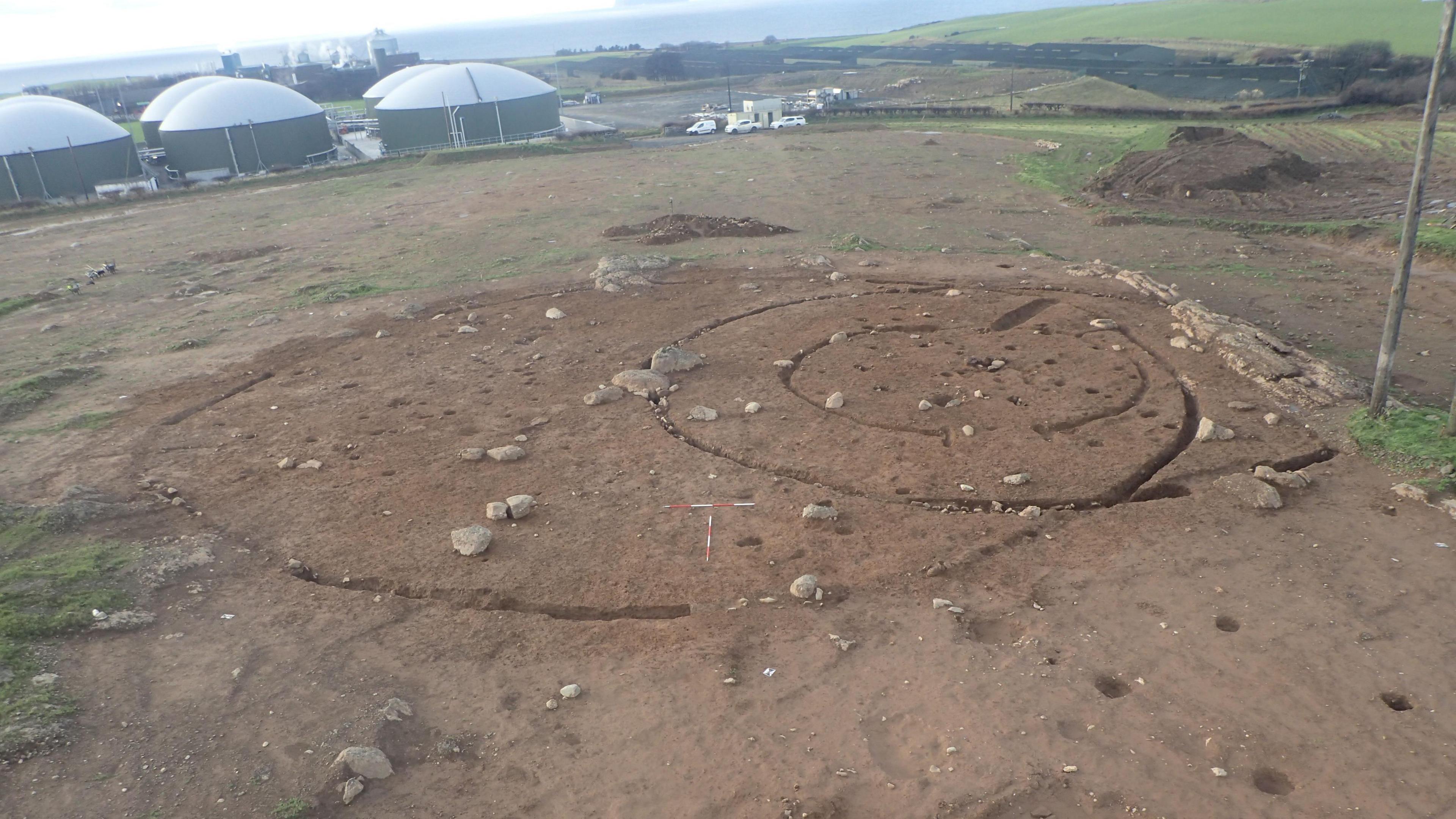 A general view of the Curragh in Ayrshire. It is muddy with a circular outline drawn out on the ground. There are silos in white and grey in the background.