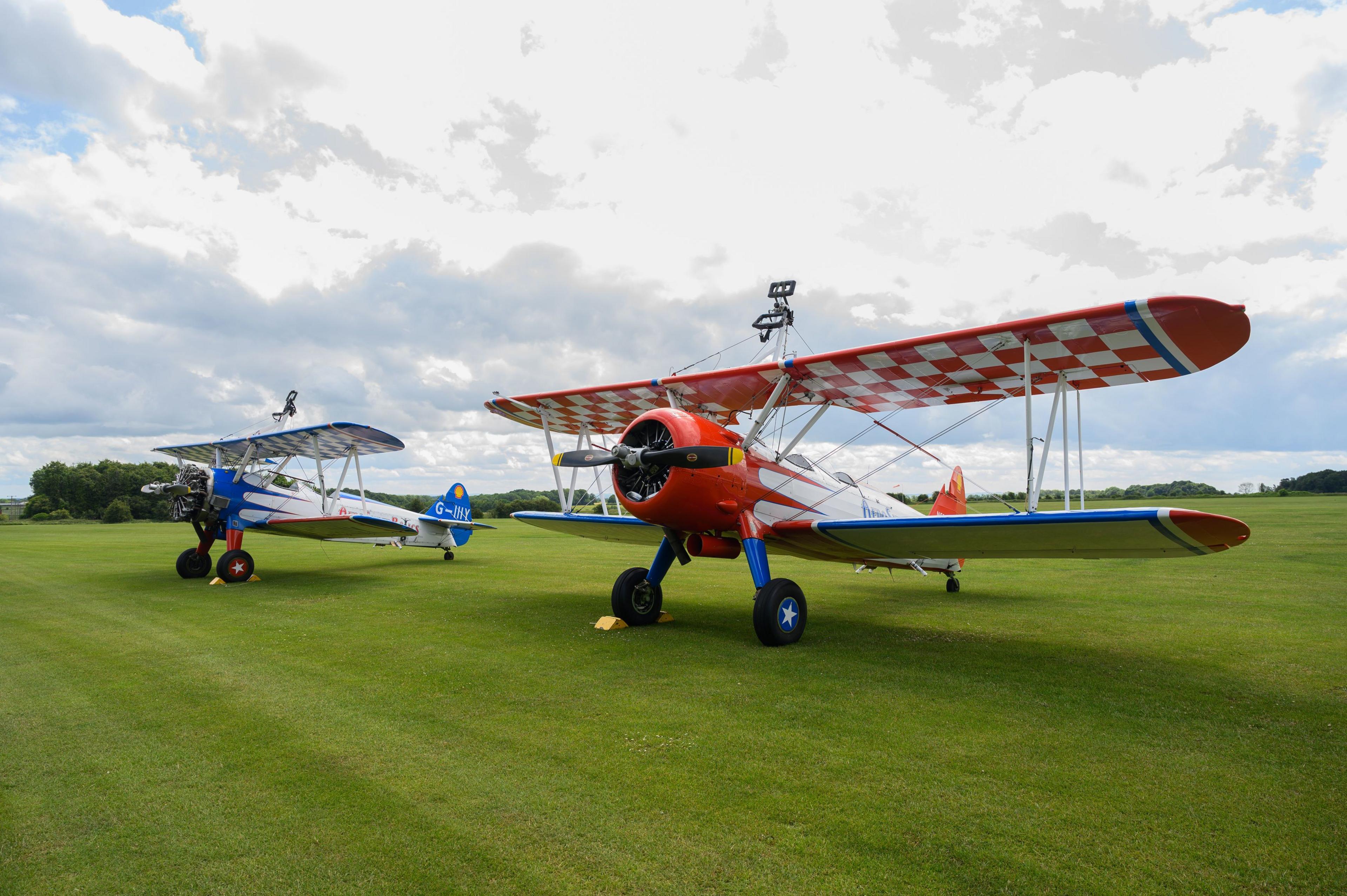 Two aeroplanes with colourful wings on green grass.