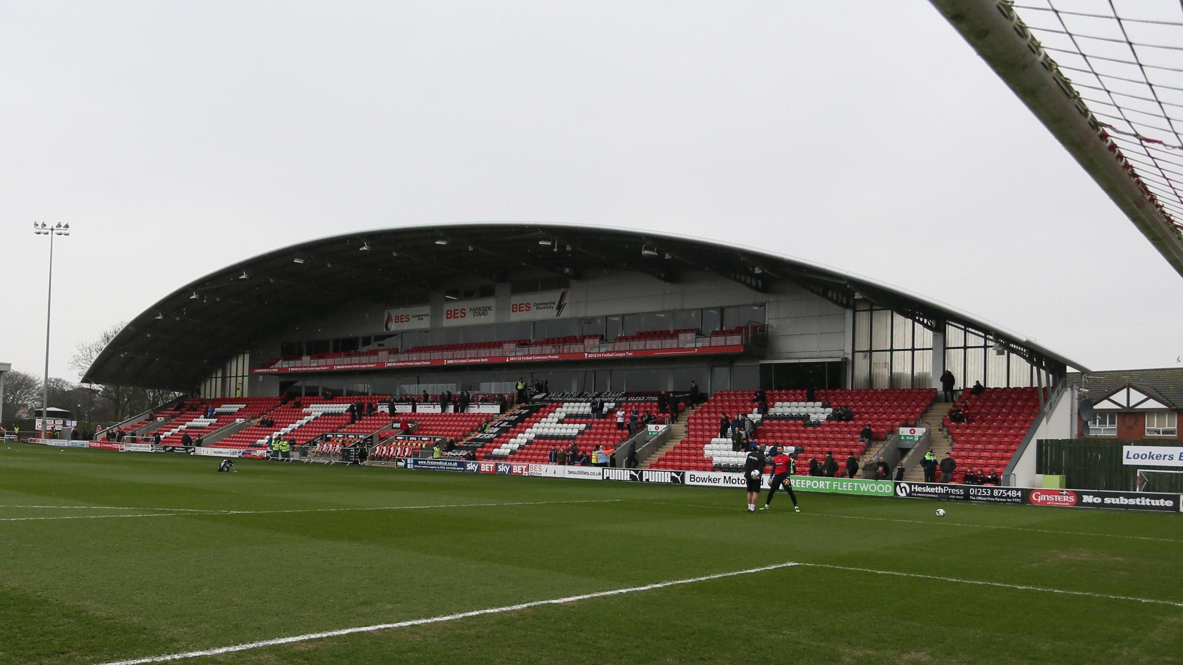 A general view of a stand at Fleetwood's stadium. It has an arched roof and is single-tier with red seats. The pitch is in front of it.