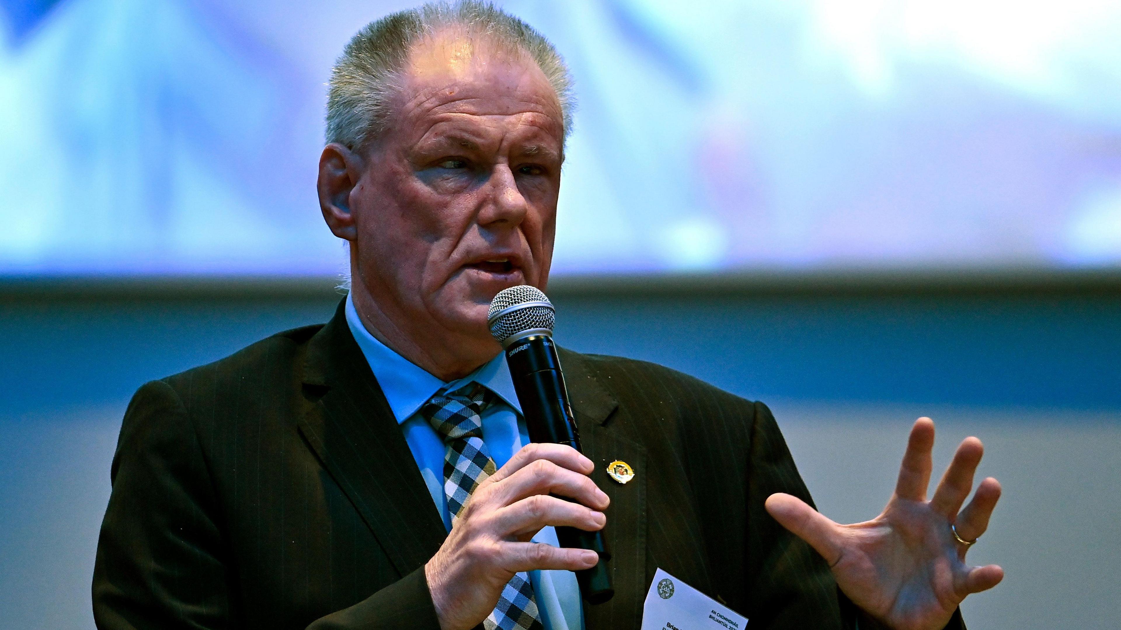 A man with grey hair holding a microphone wearing a suit