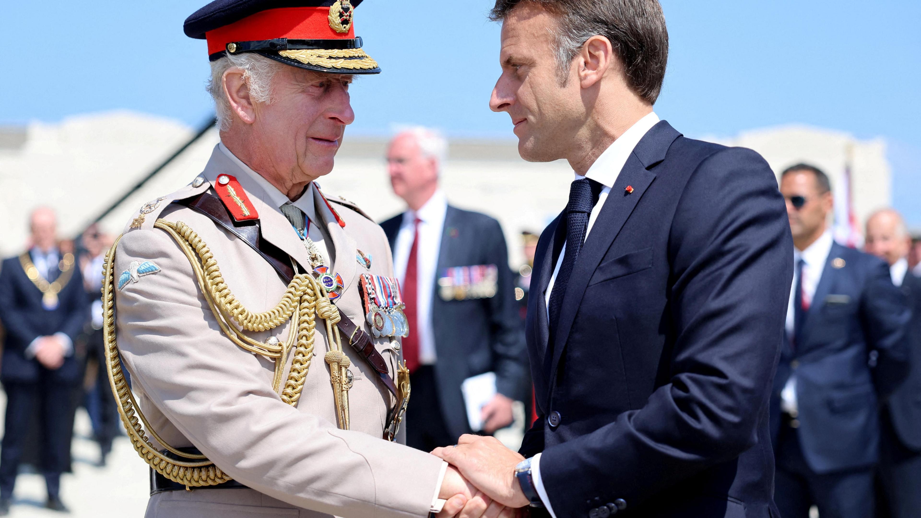 President Macron and King Charles, wearing badges and uniform, shaking hands in a meeting in 2024.