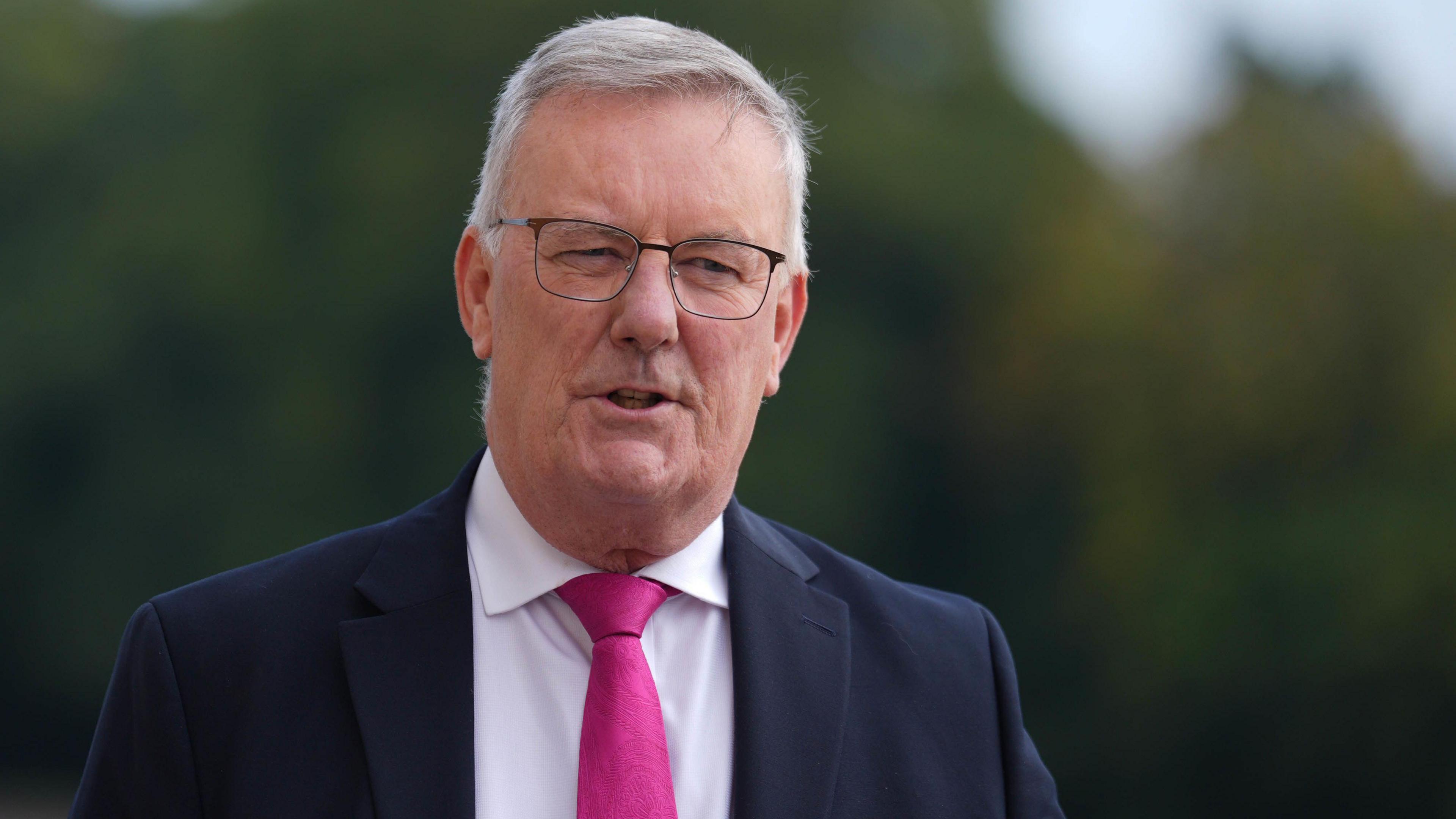 Mike Nesbitt, with short grey hair, wearing a navy suit, white shirt, pink tie and glasses.