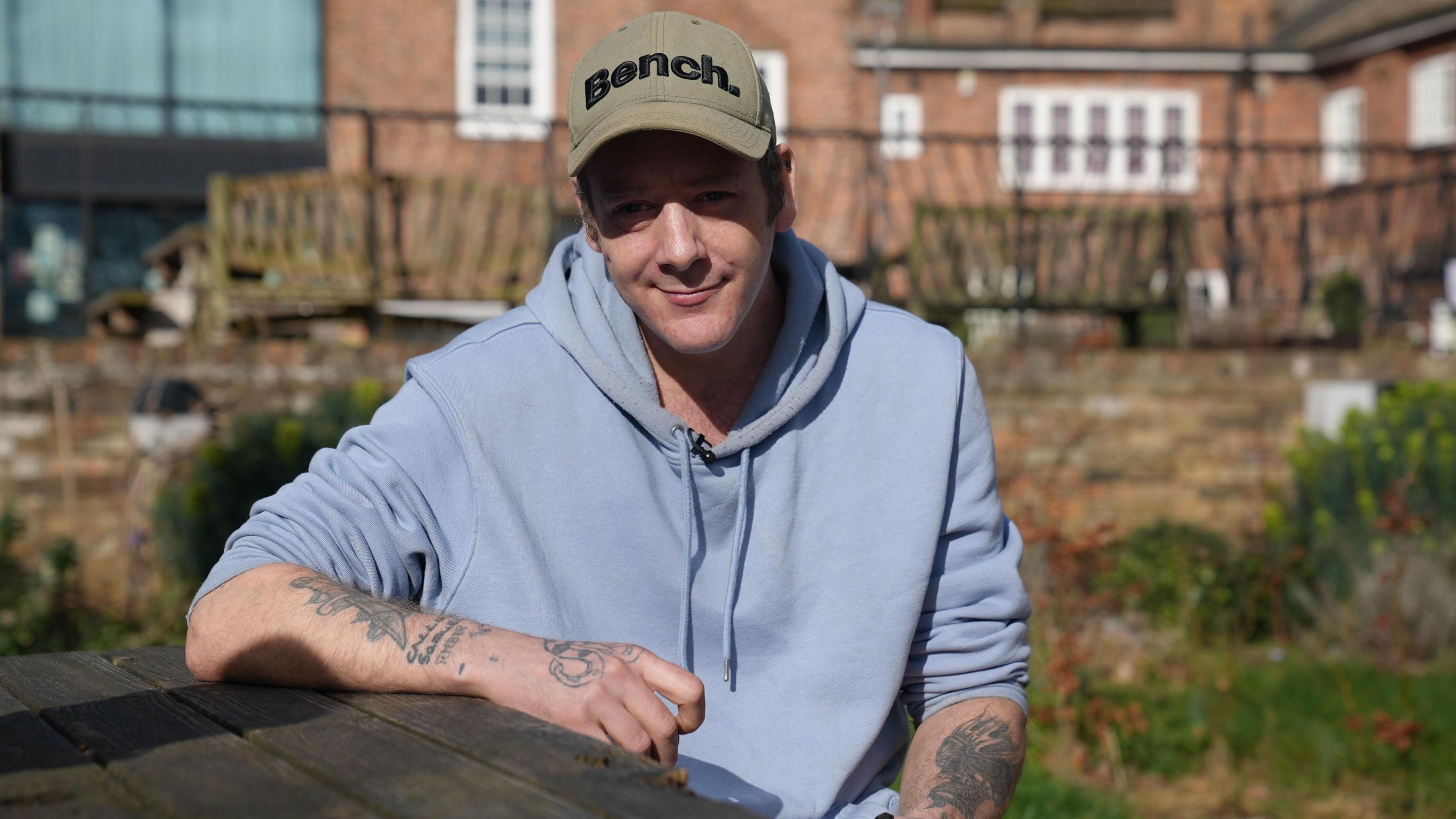 David sitting at a wooden picnic table in The Ferry Project's garden