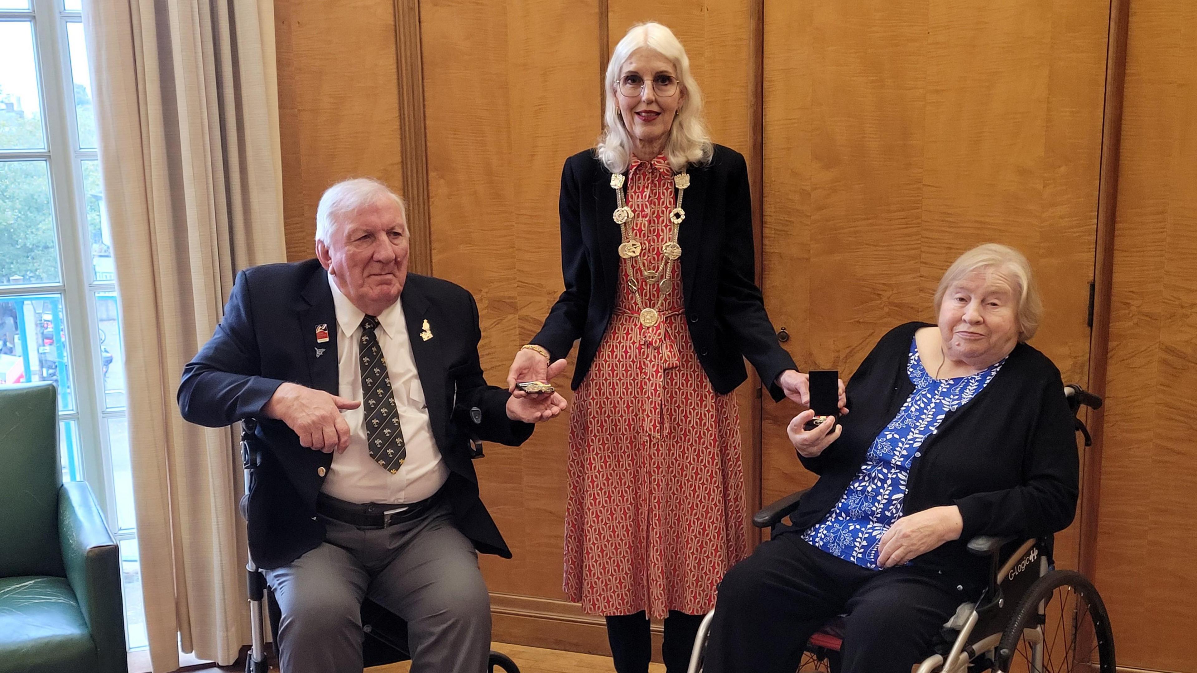 David Freeman and Pam Carman holding medals and sitting either side of Lord Mayor Vivien Thomas, who remains standing.