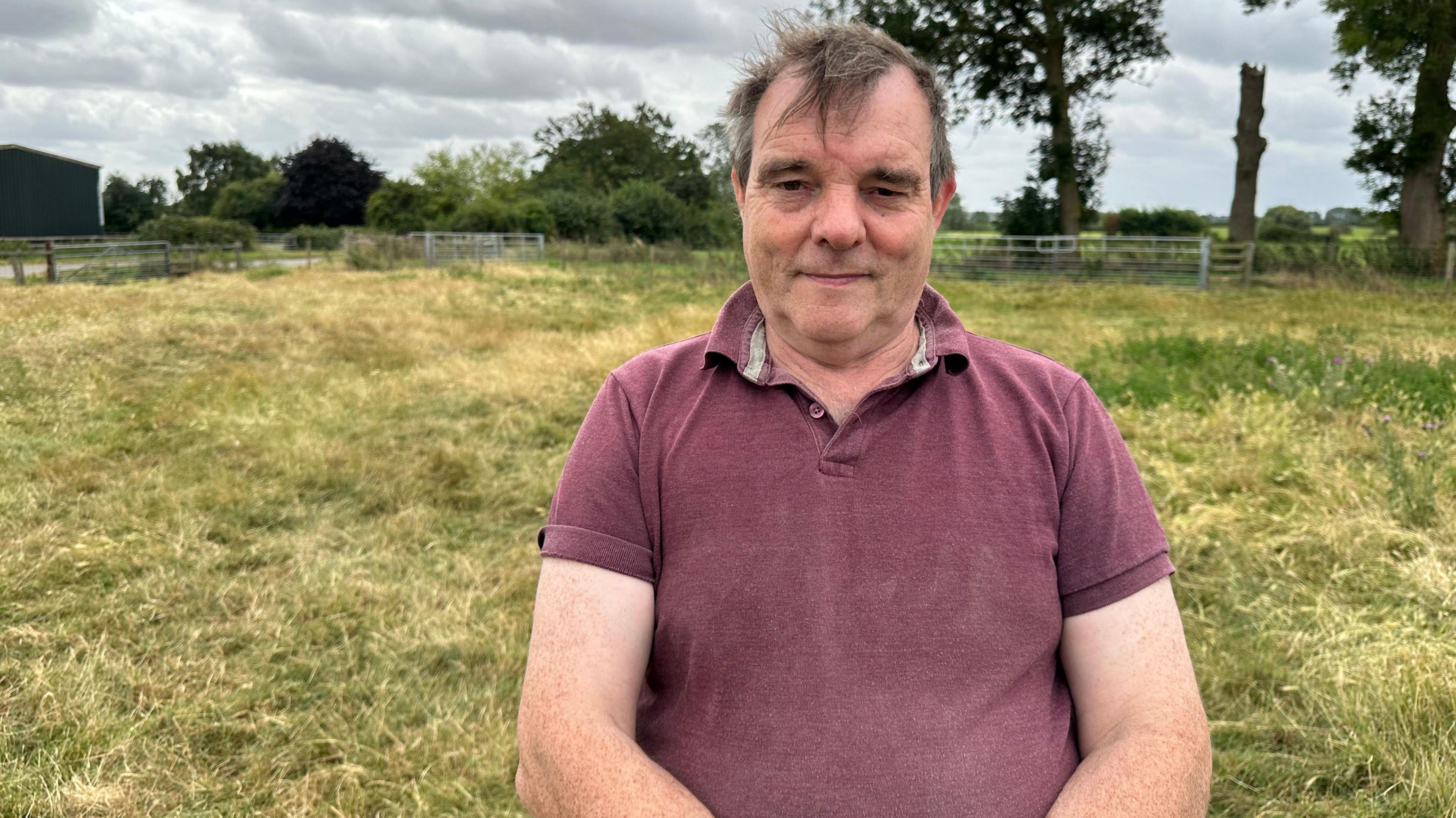 A man in a purple t shirt stands in a field