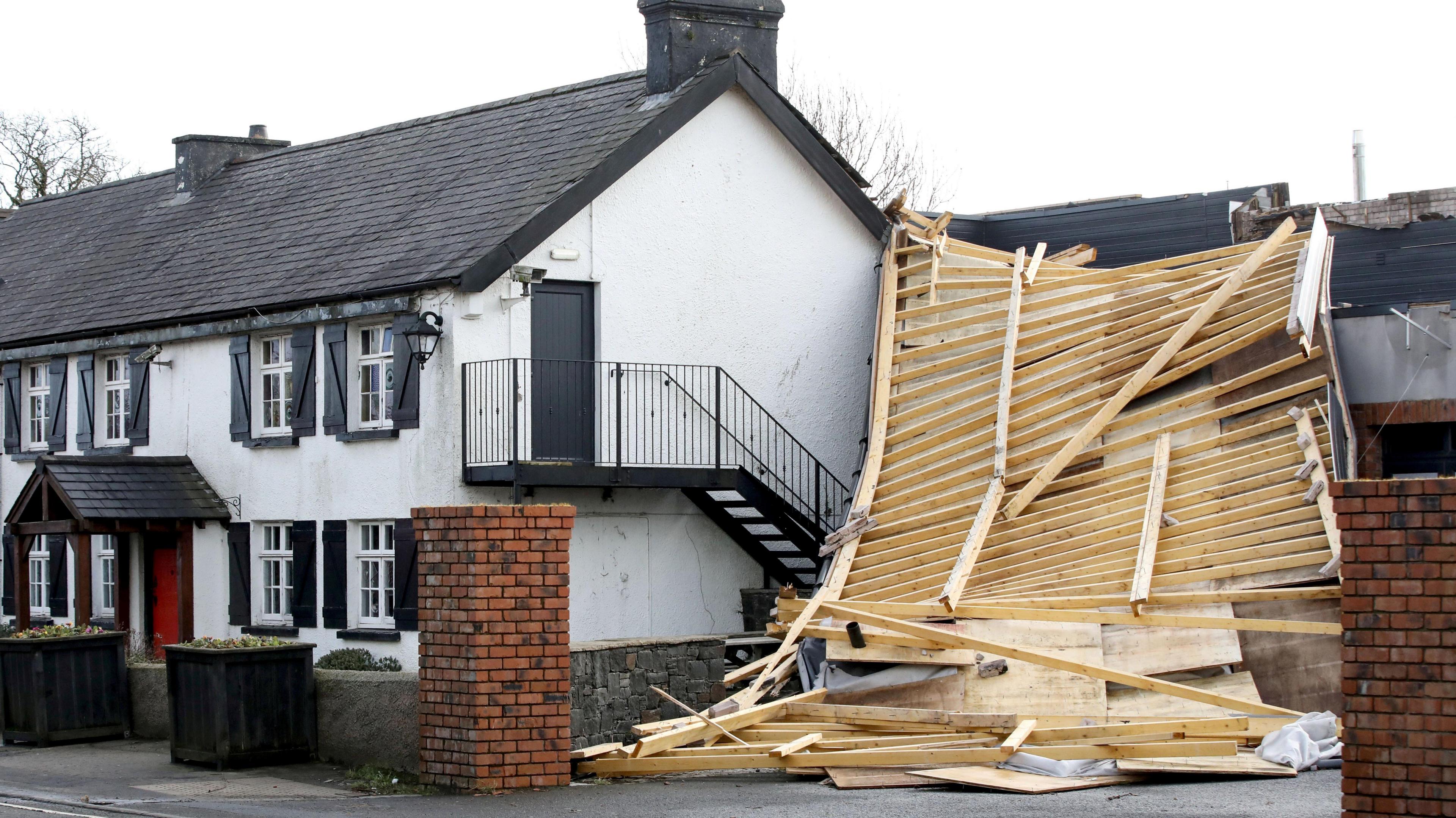 A large part of a roof has been torn off from a hotel. Wooden beams are lying about from the roof to the ground.