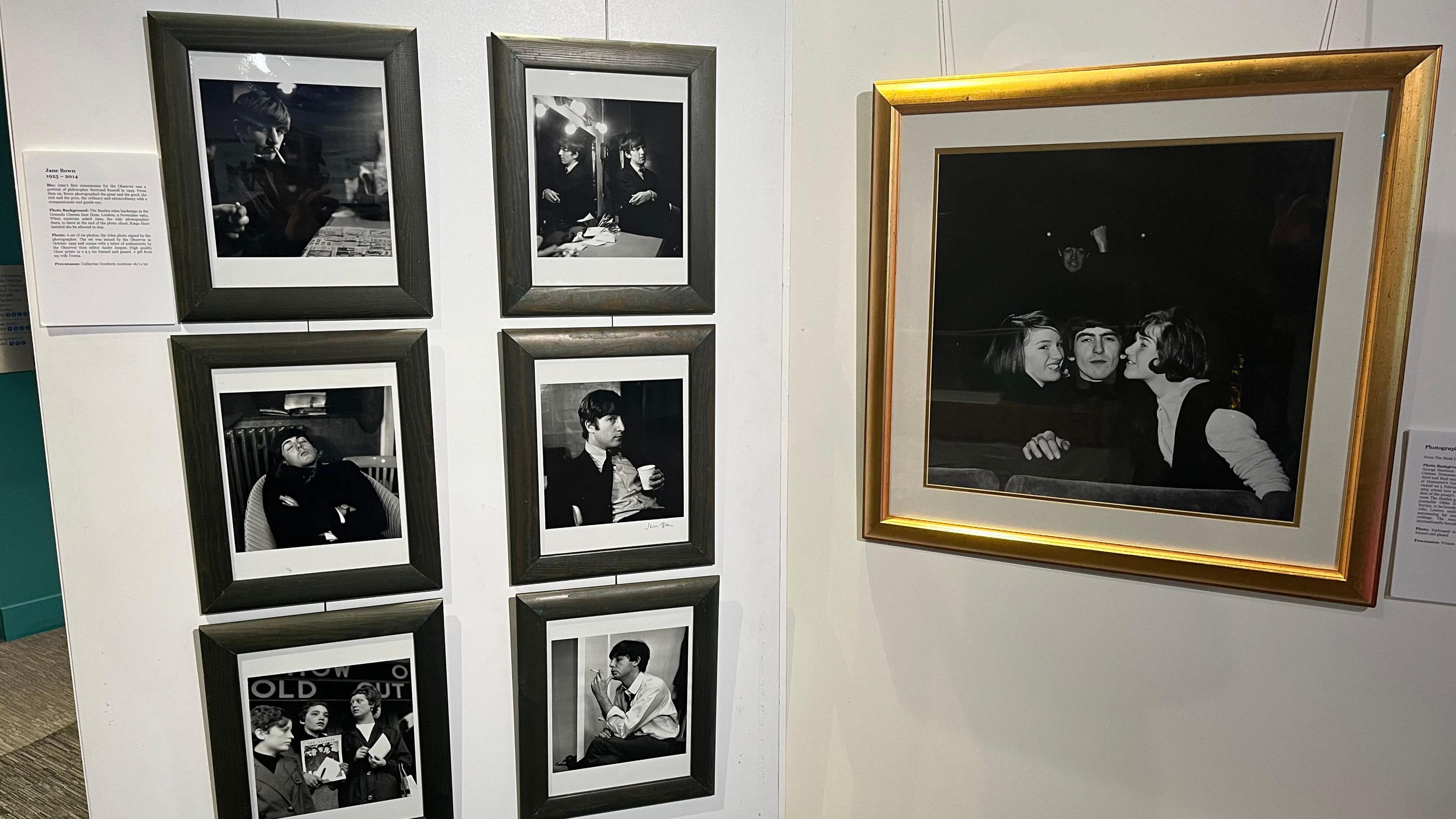Six smaller photos are shown on the left of a display alongside a larger photo on the right, showing members of The Beatles in black and white images at an exhibition.