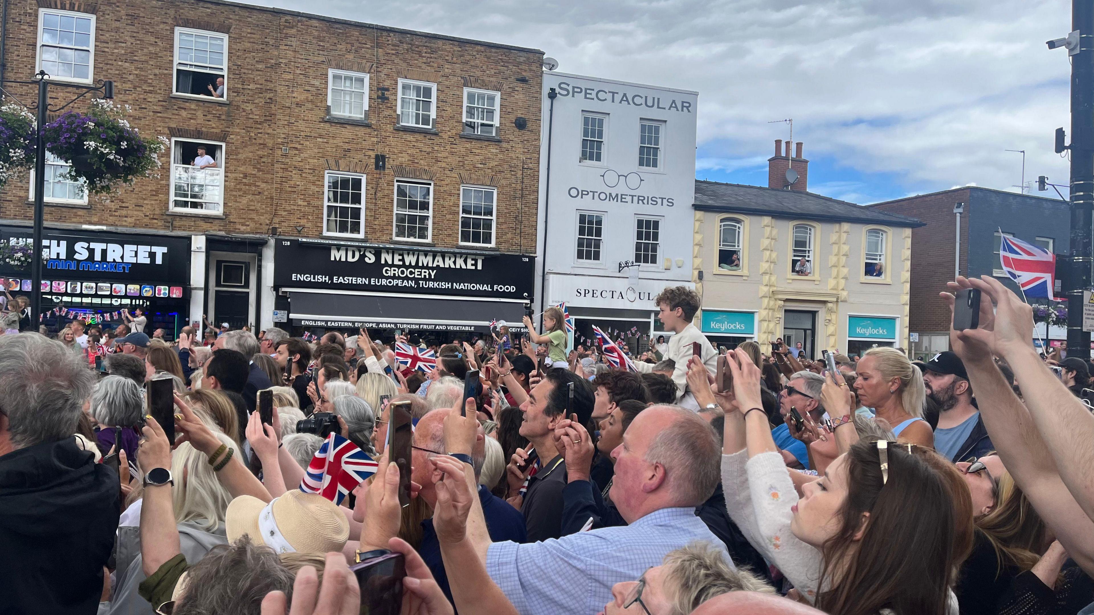 A large crowd of people look away from the camera, many of people with phones in their hands to take pictures.