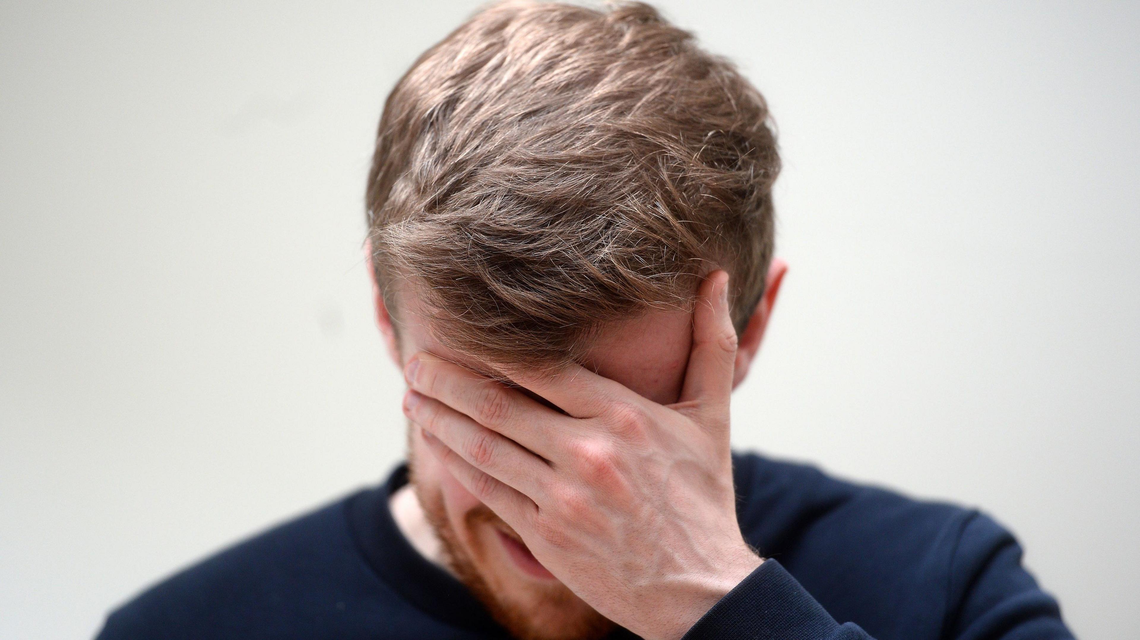 Stock image of a man with his hand on his head - it appears he is in pain - possibly suffering from a headache or migraine