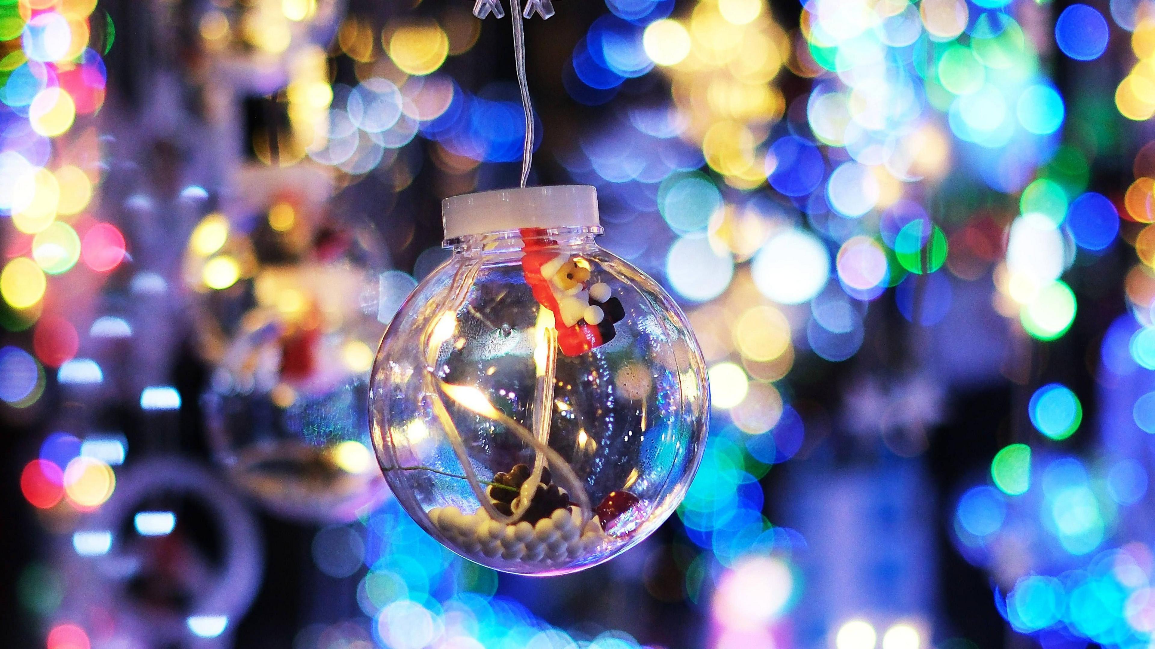 A glass bauble with a small Father Christmas inside it hangs in front of colourful lights.