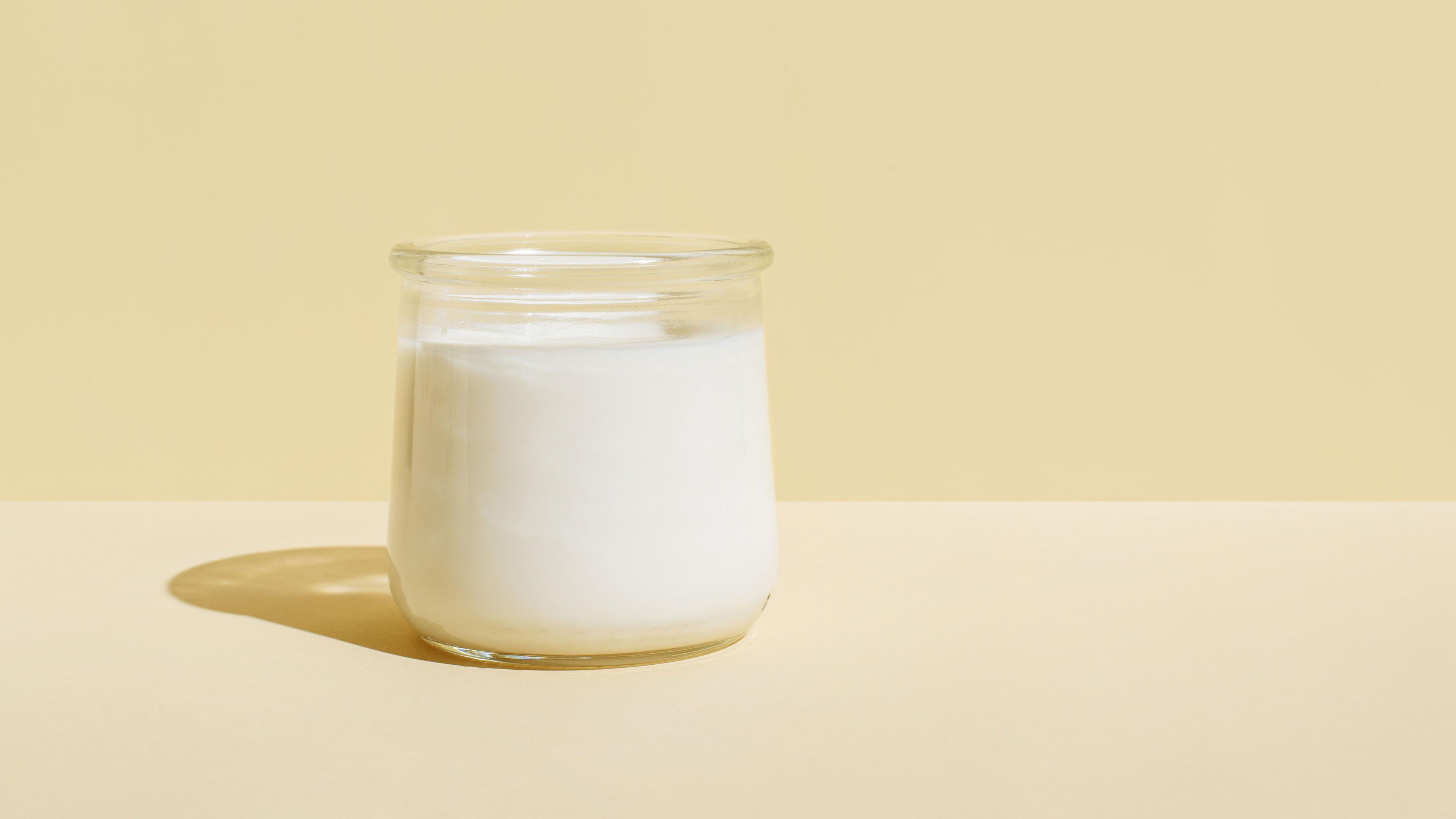 A glass pot of plain yoghurt on a pale yoghurt background.