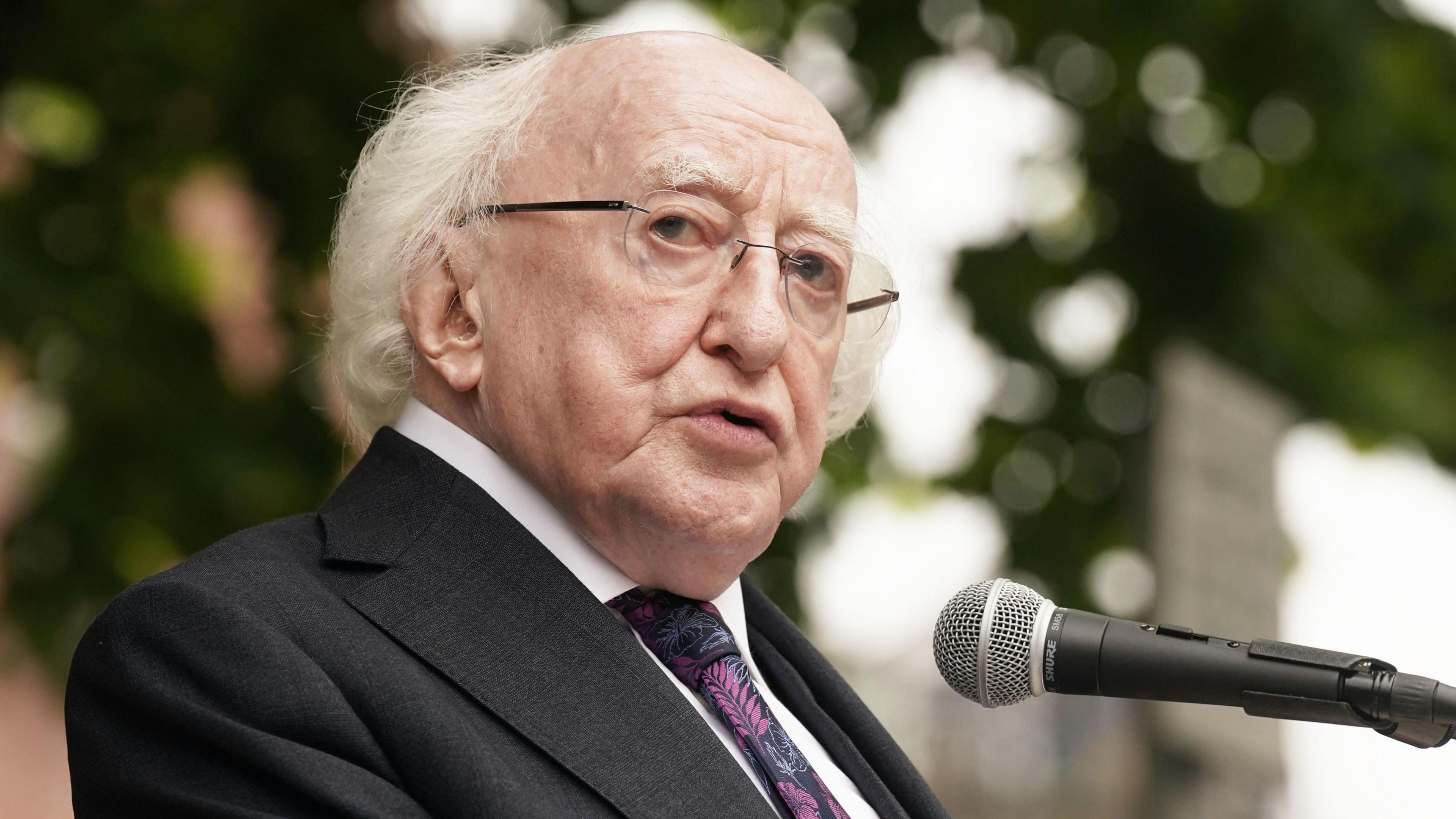 Michael D Higgins speaking at a microphone. He is wearing a suit a tie