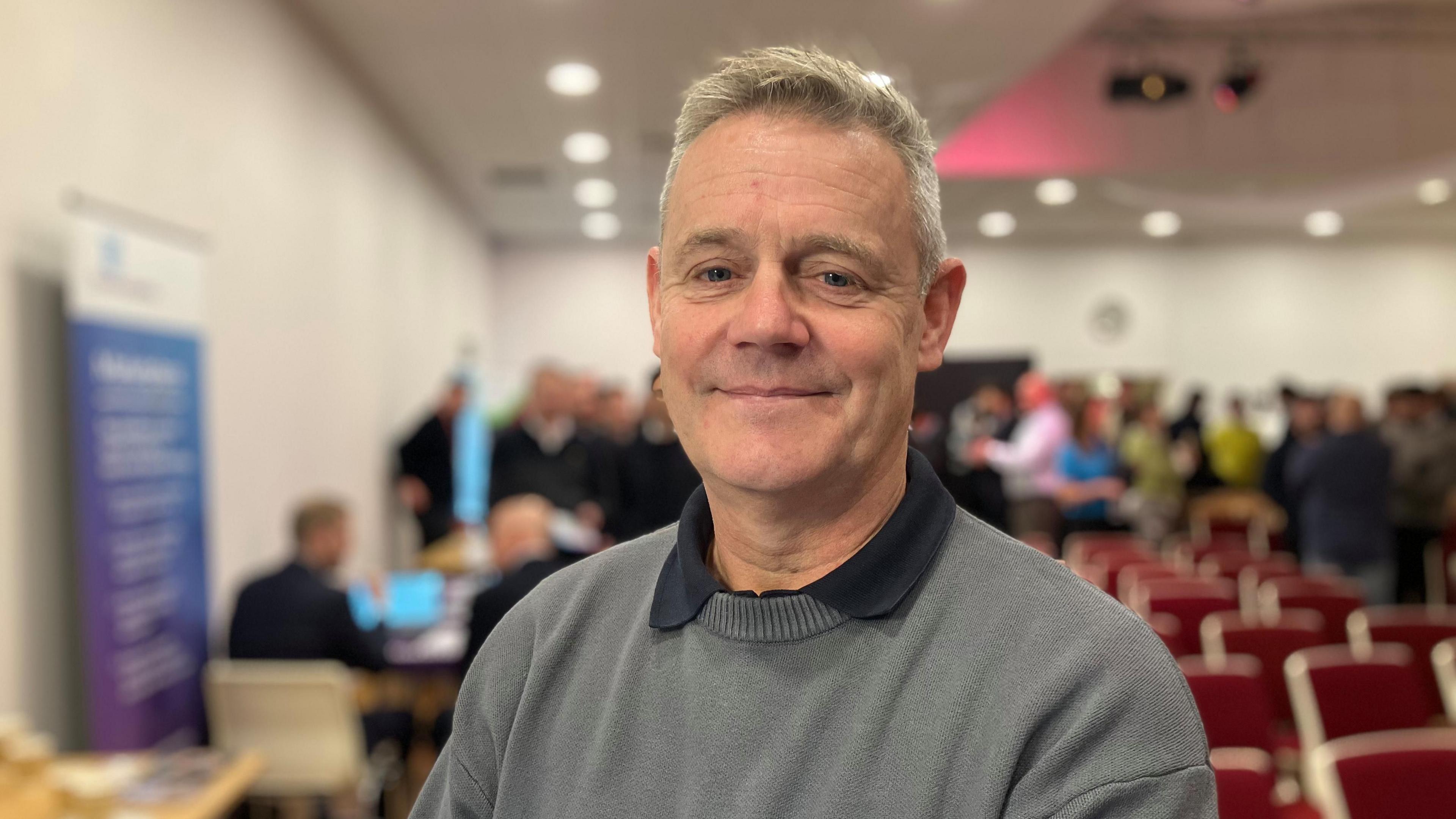 A man in a grey jumper in a conference room