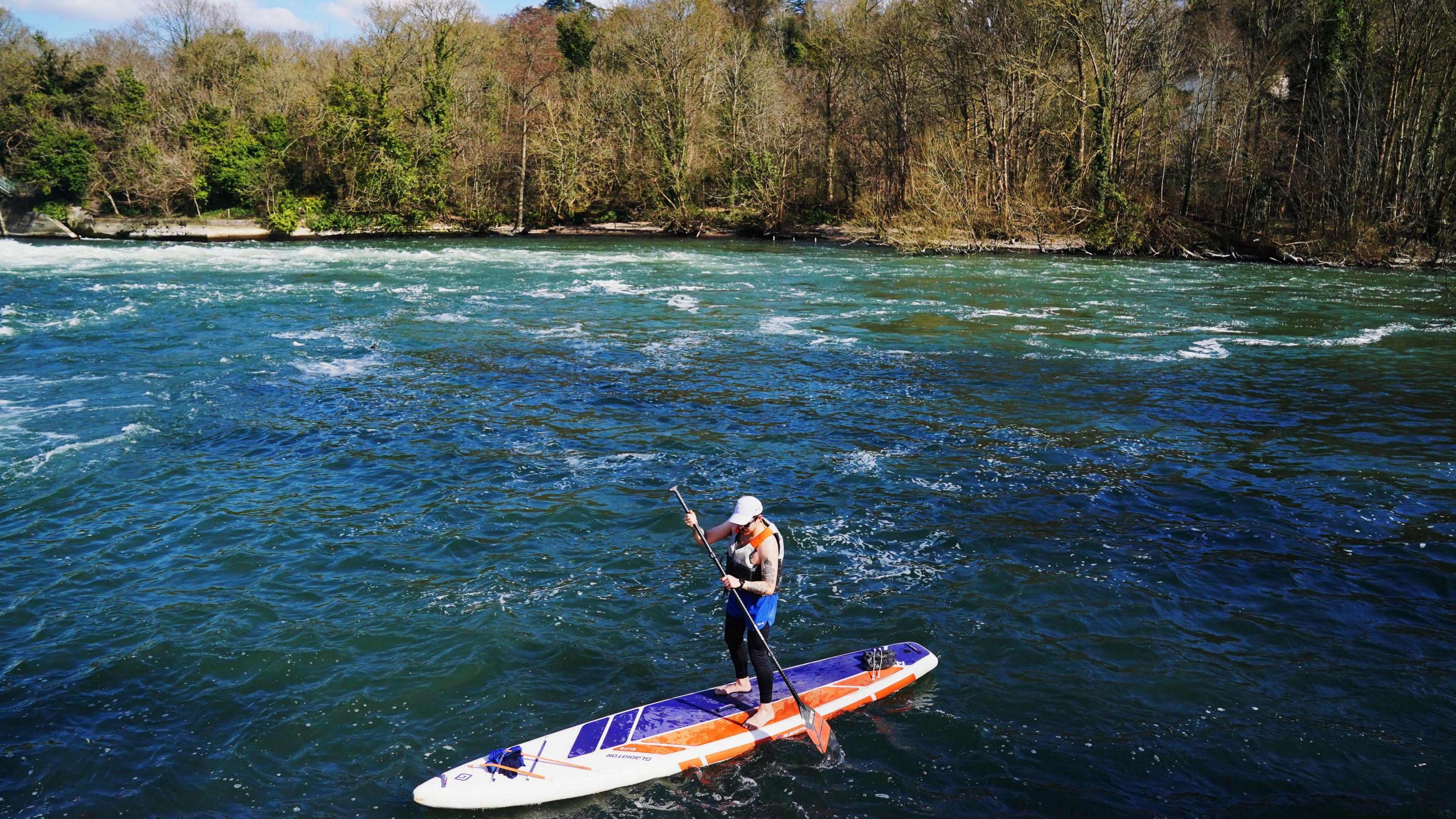 A paddleboarder bathed in sunshine on a river with trees in the background