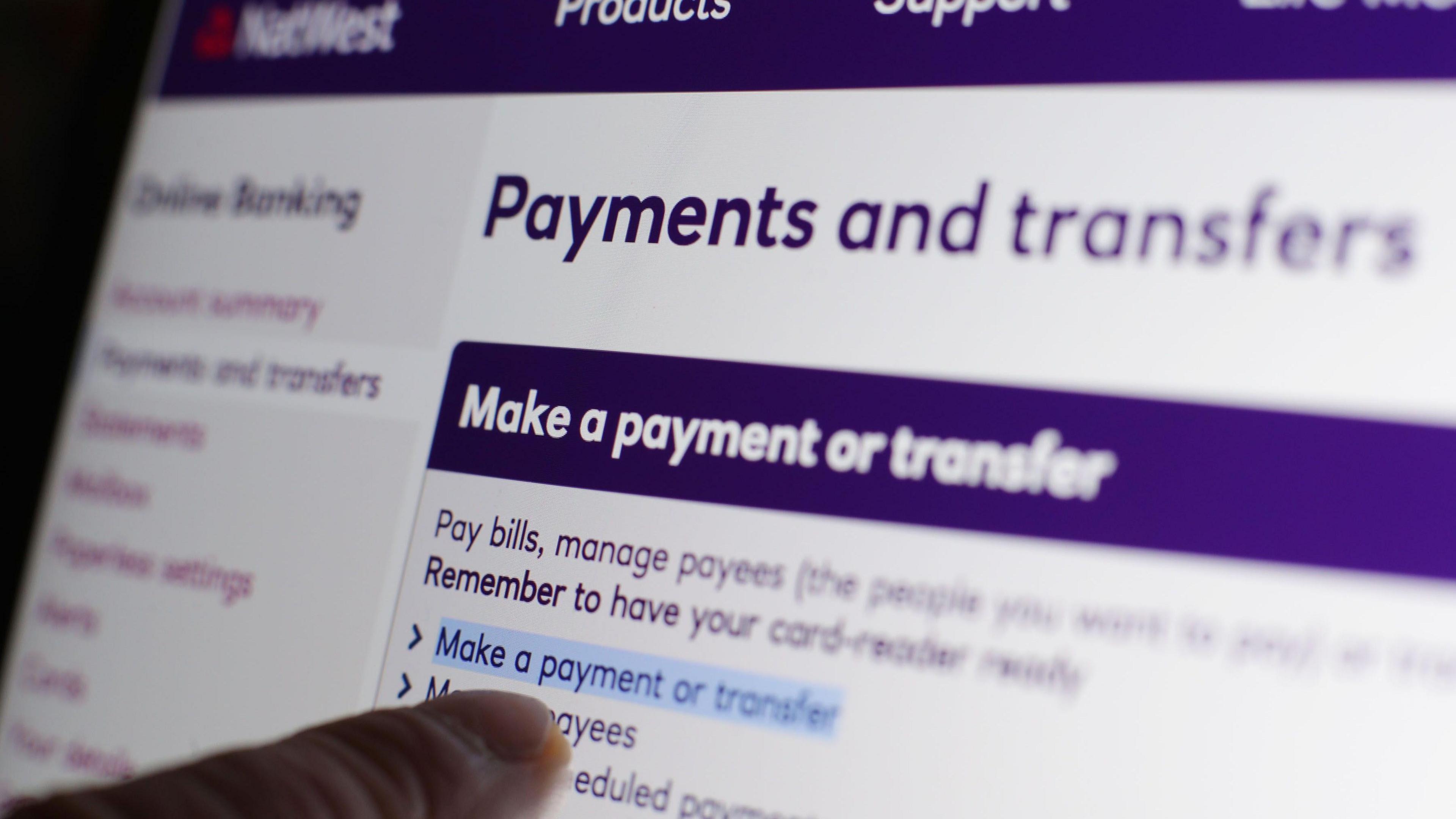 A finger pointing at a banking screen - towards a highlighted area that says "Make a payment or transfer"