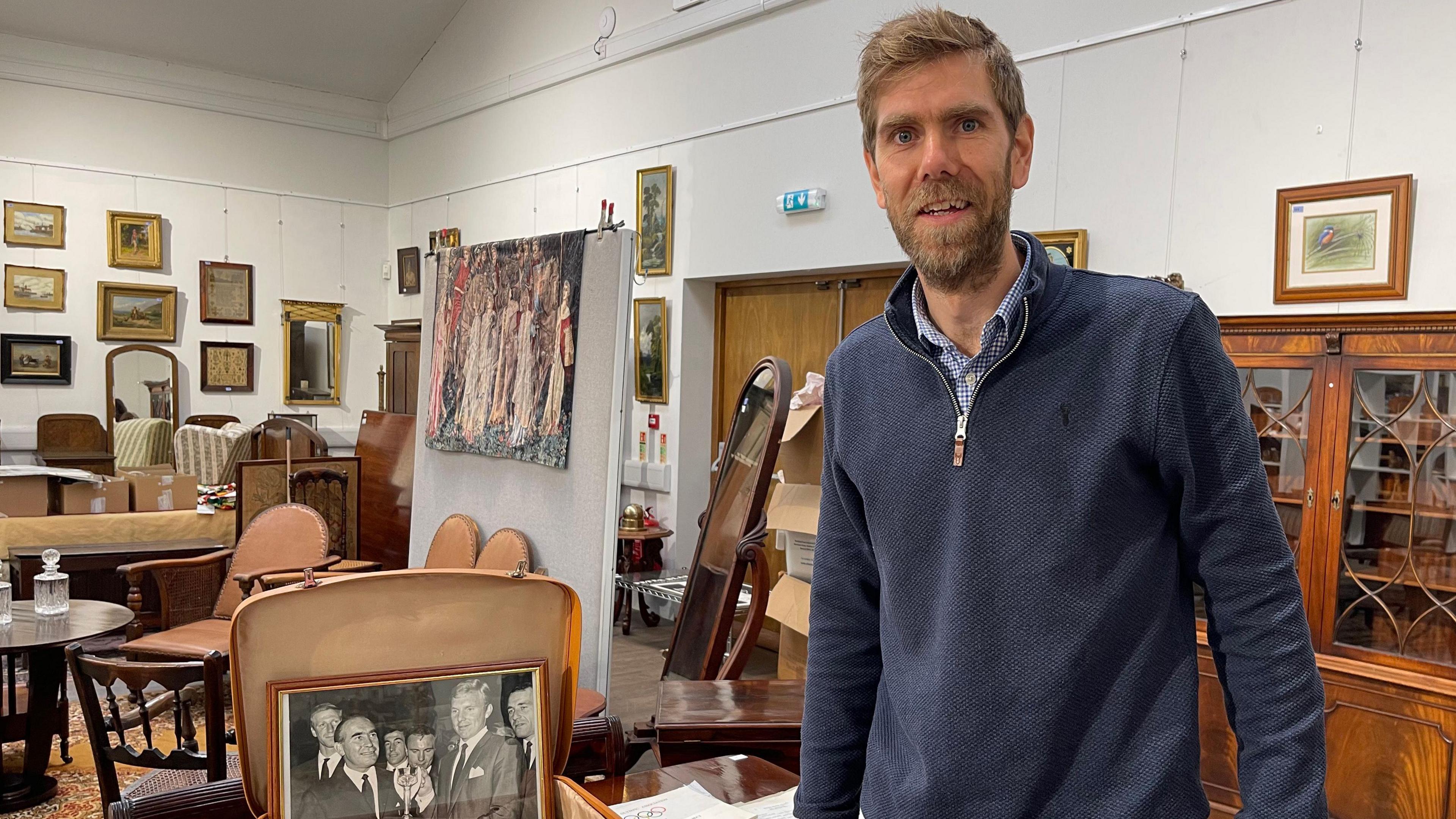 A man standing dressed in blue stood adjacent to the suitcase of memorabilia 