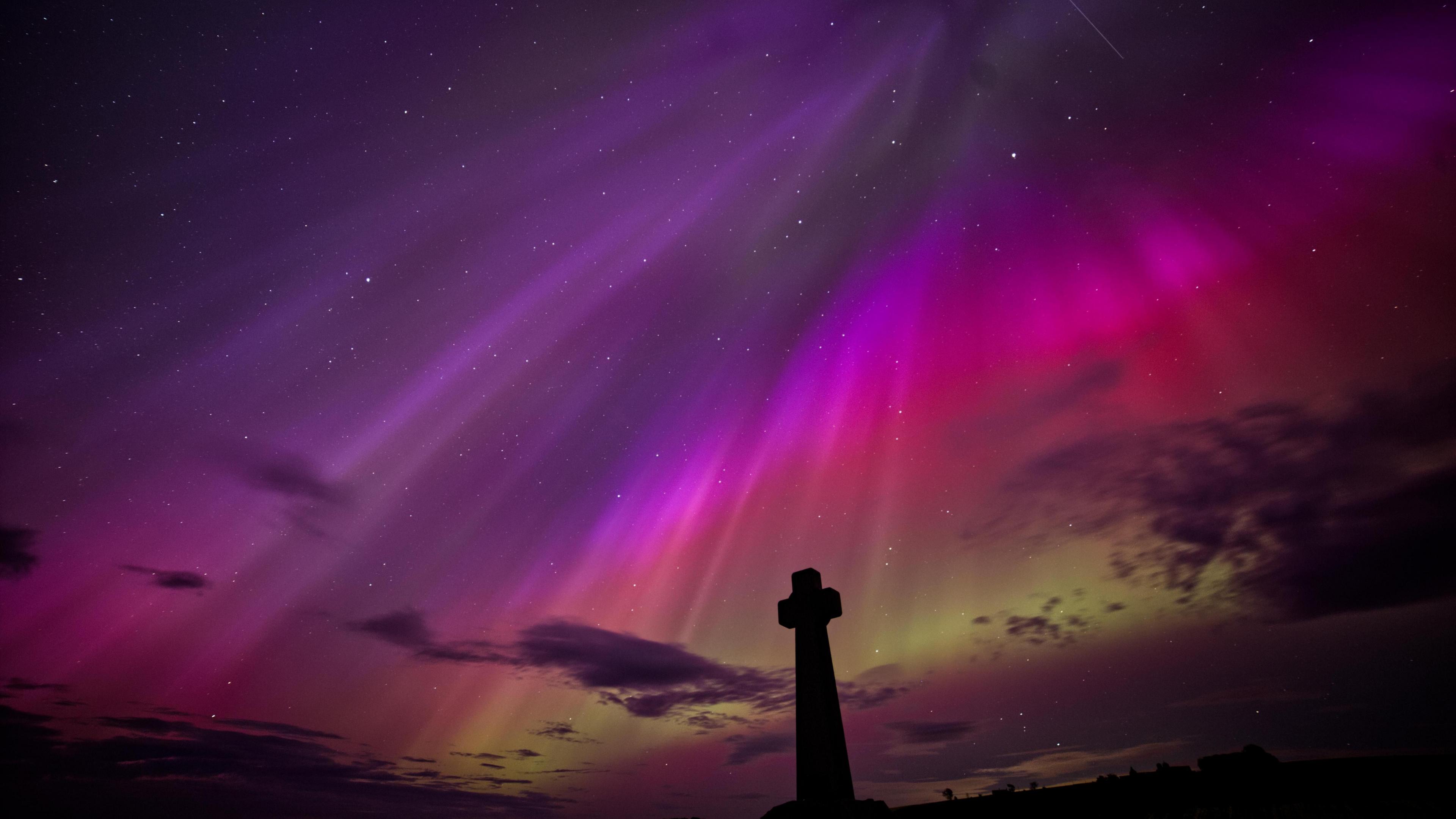 A stone cross beneath coloured skies