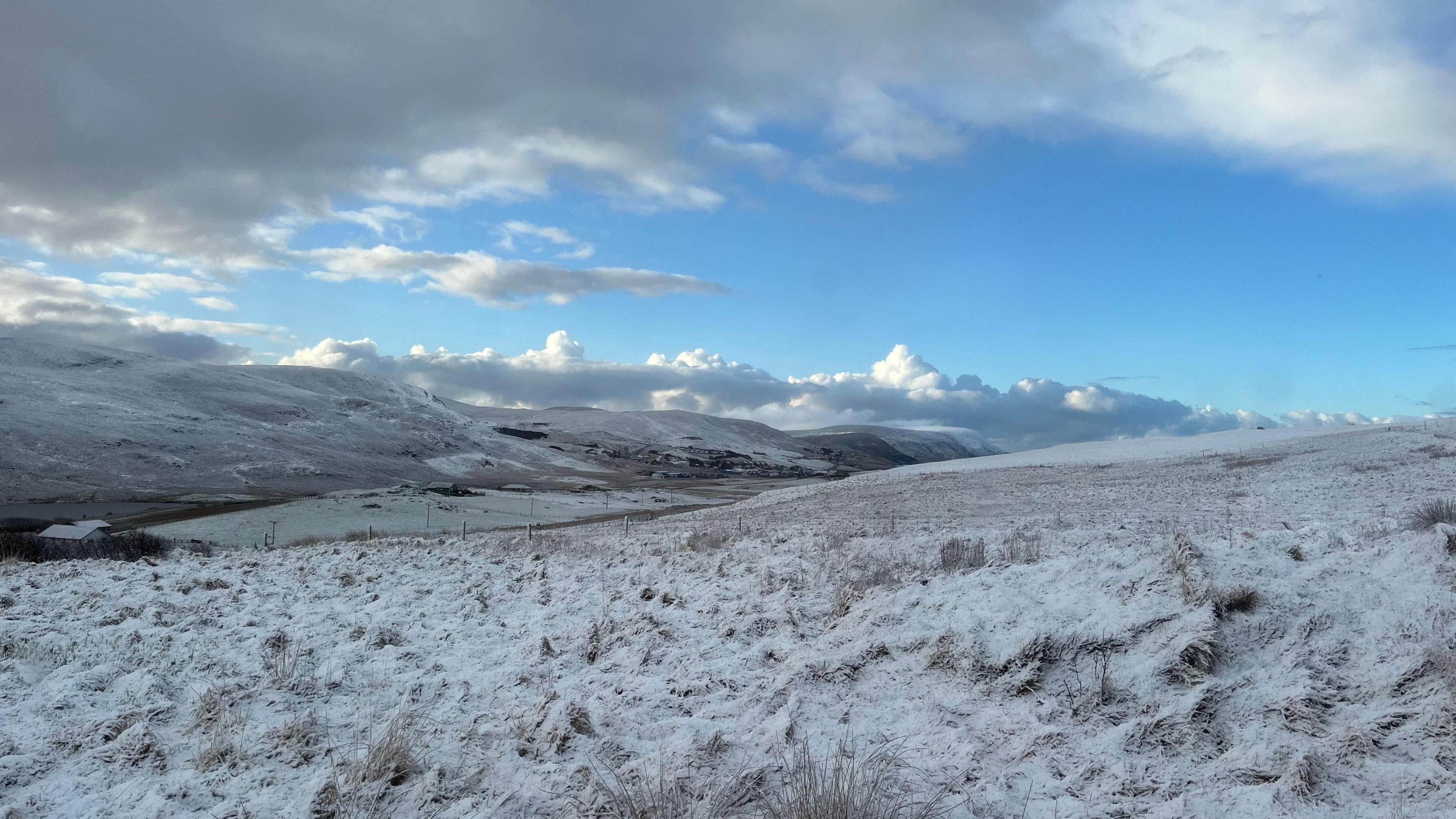 Snow covers hills and land over Shetland. Partially cloudy skies above. 
