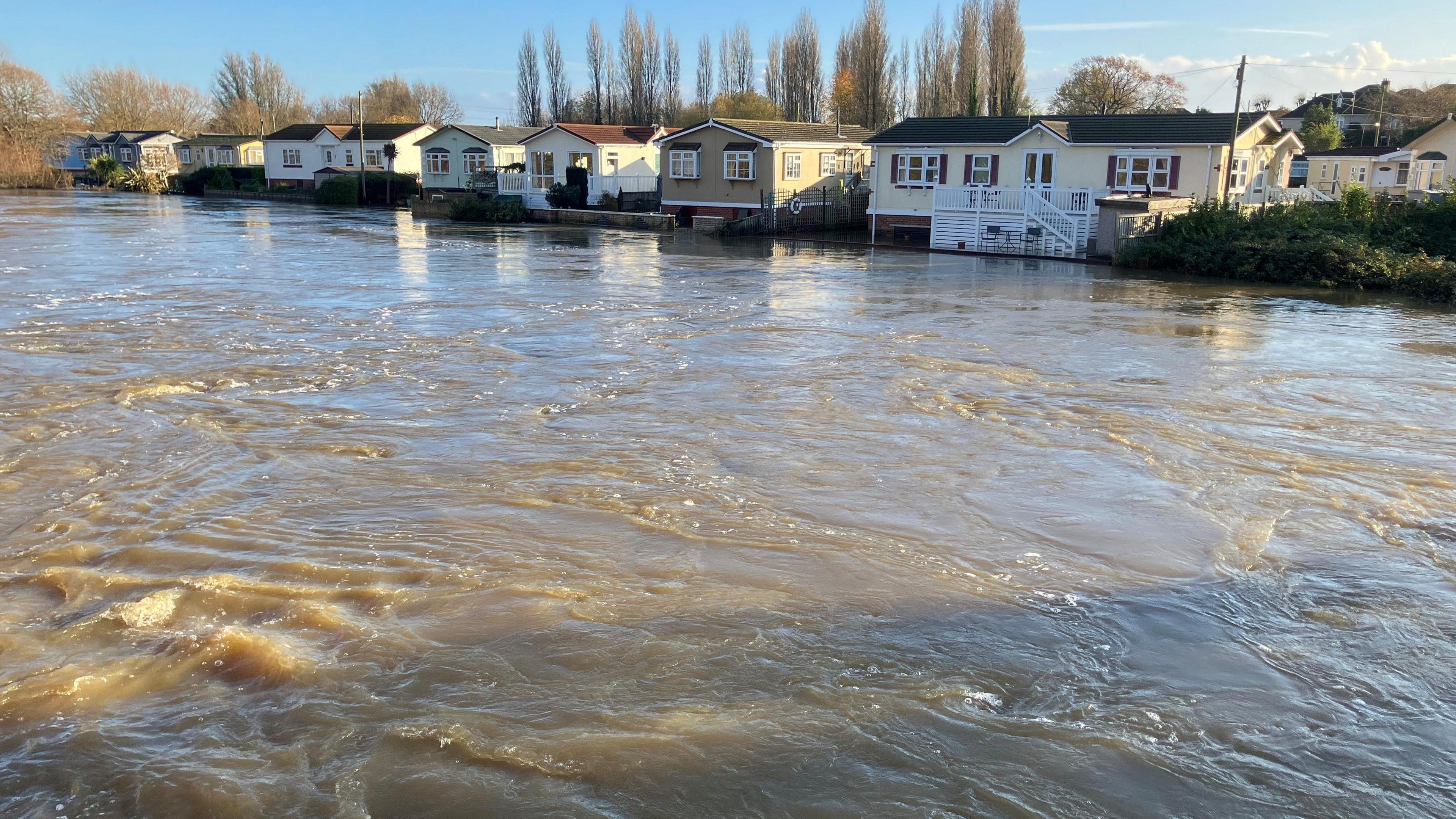 The River Stour at a very high level with a row of mobile homes at the far side of the river