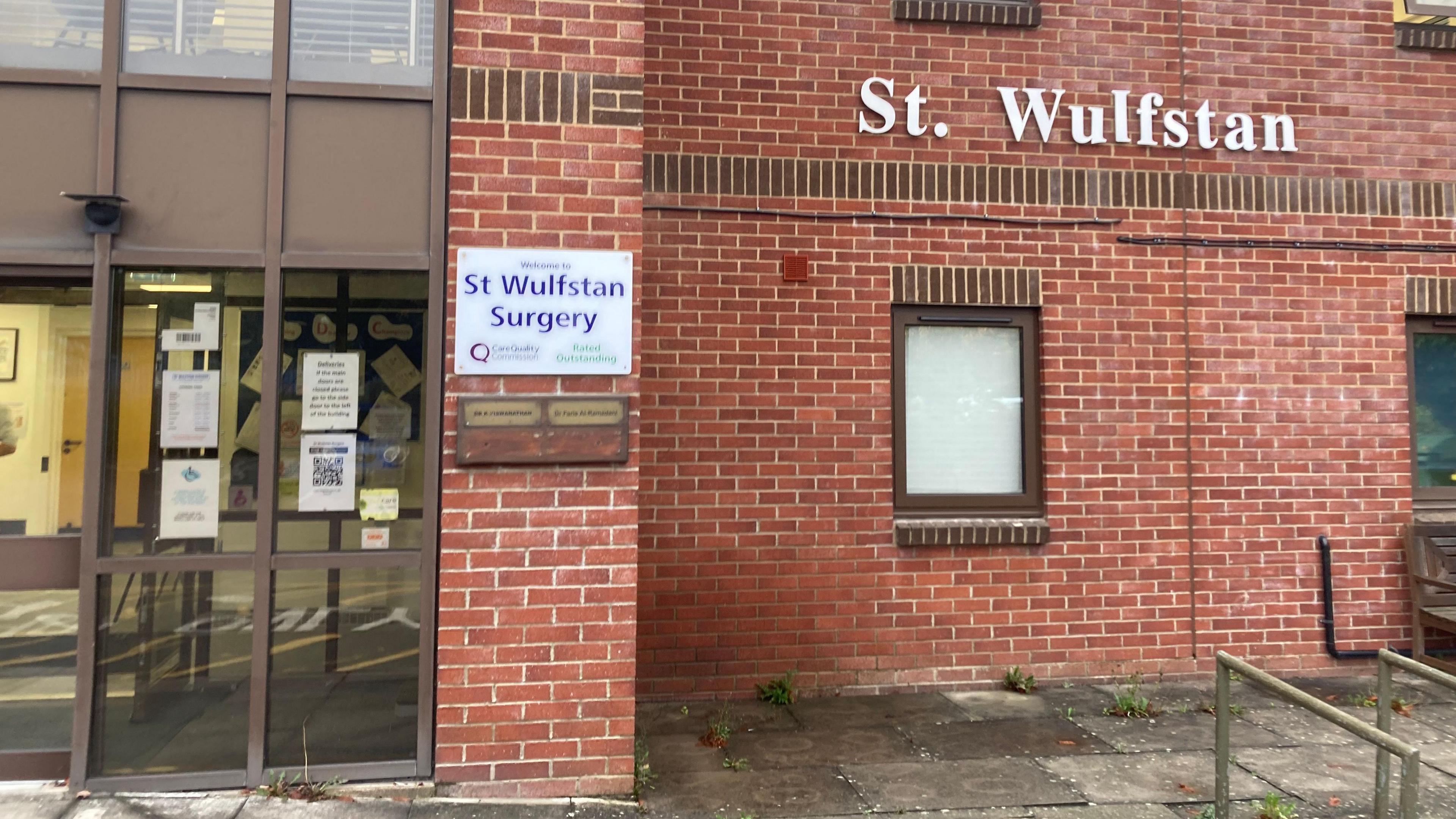 The outside of St Wulfstan Surgery, a red brick building with a brown framed window and glass doors.