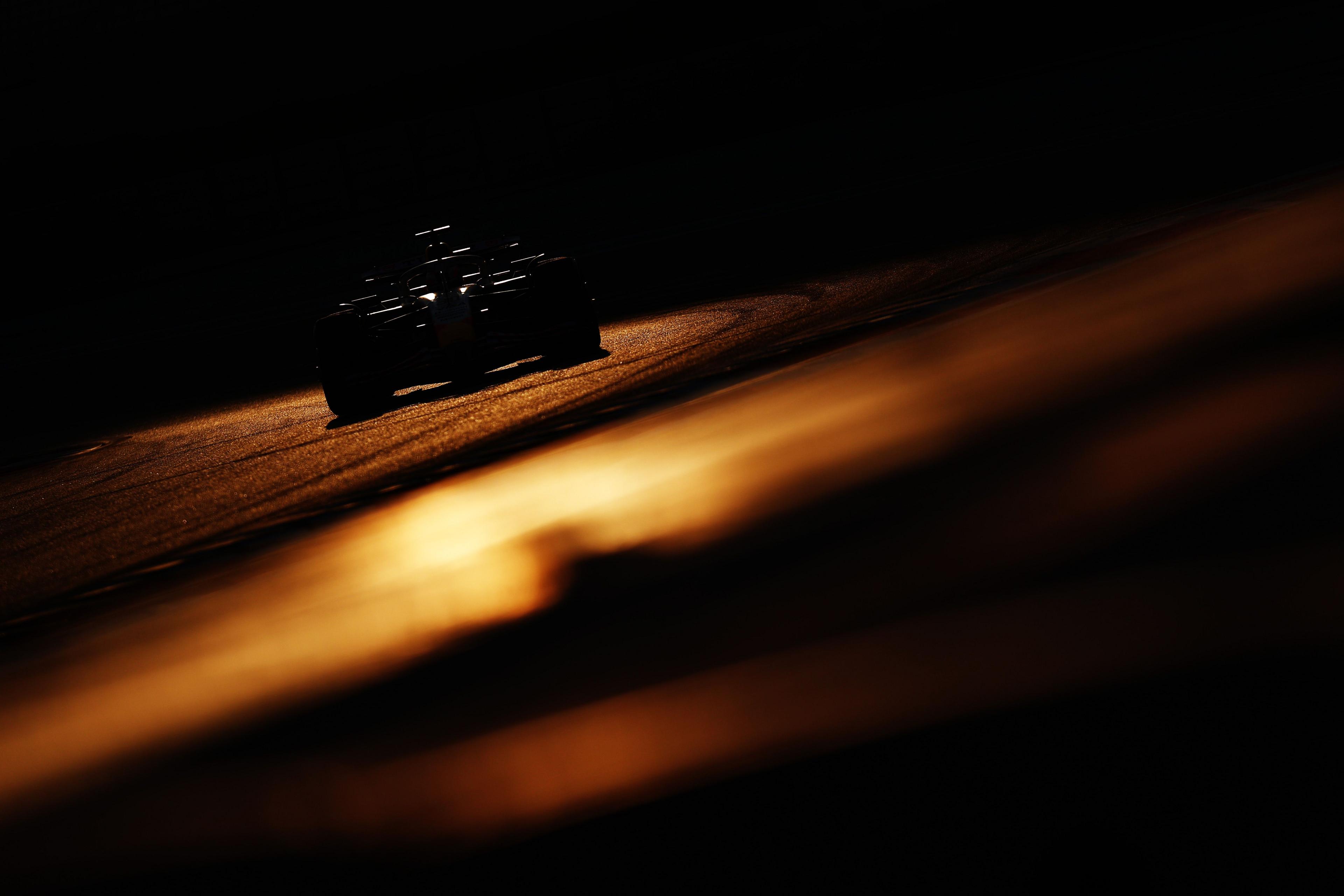 Un coche de Fórmula 1 recortado circula por una pista al atardecer, con la tenue luz dorada reflejándose en el asfalto y creando una escena dramática y de alto contraste.