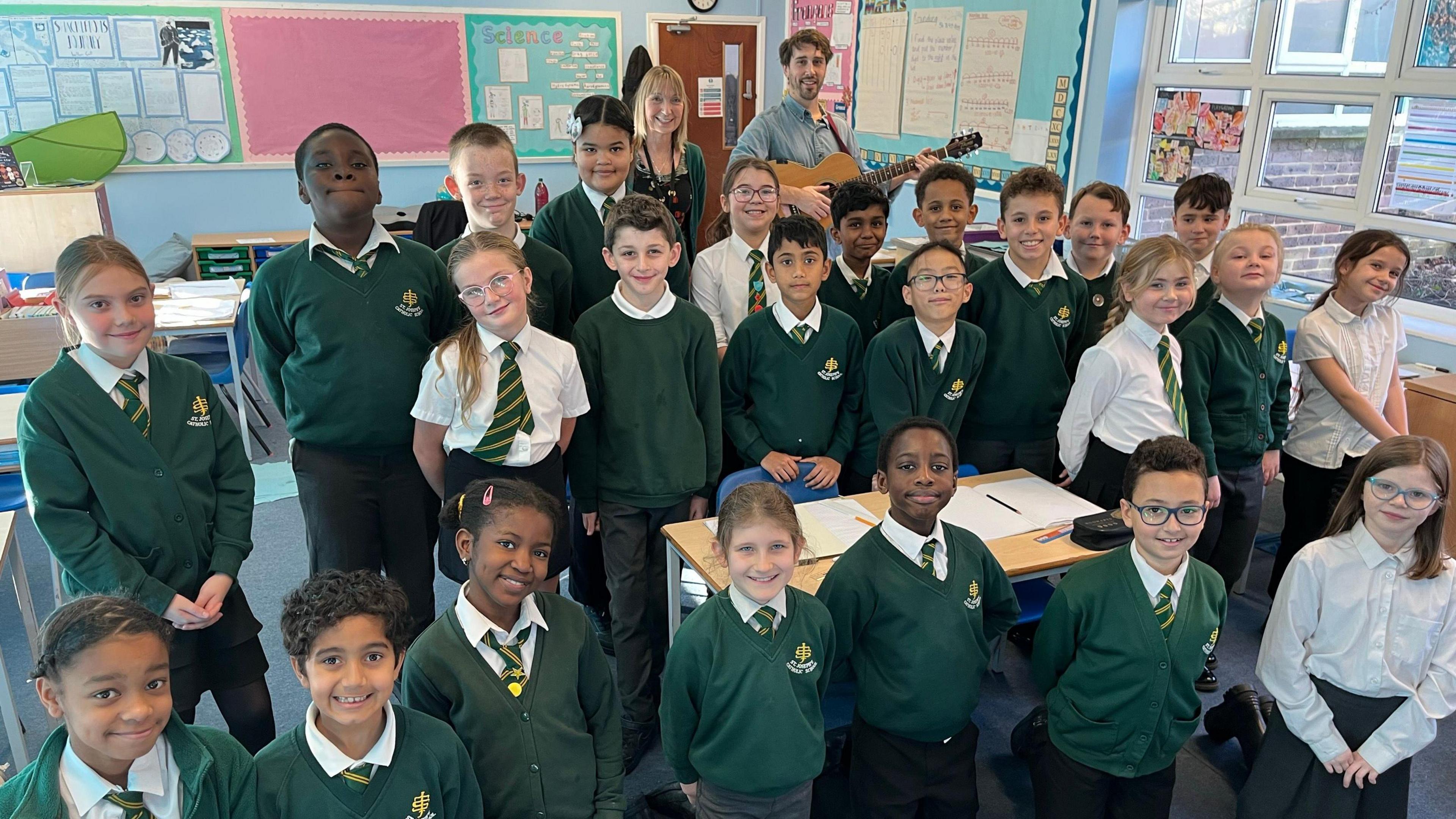 Children from St Josephs' Primary School in their classroom with their headteacher behind and teacher holding a guitar after performing their Christmas re-write of Nazareth