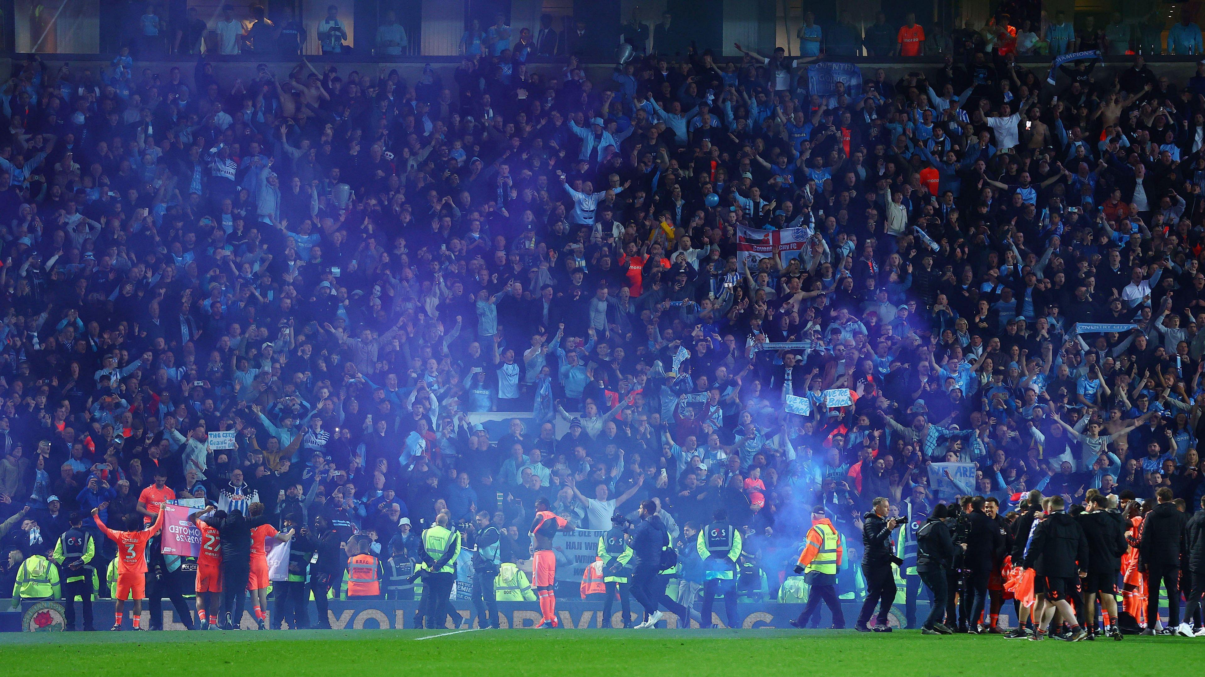 Coventry players celebrate with their travelling fans at Blackburn after securing promotion, with blue smoke from a flare drifting across the pitch from the stands